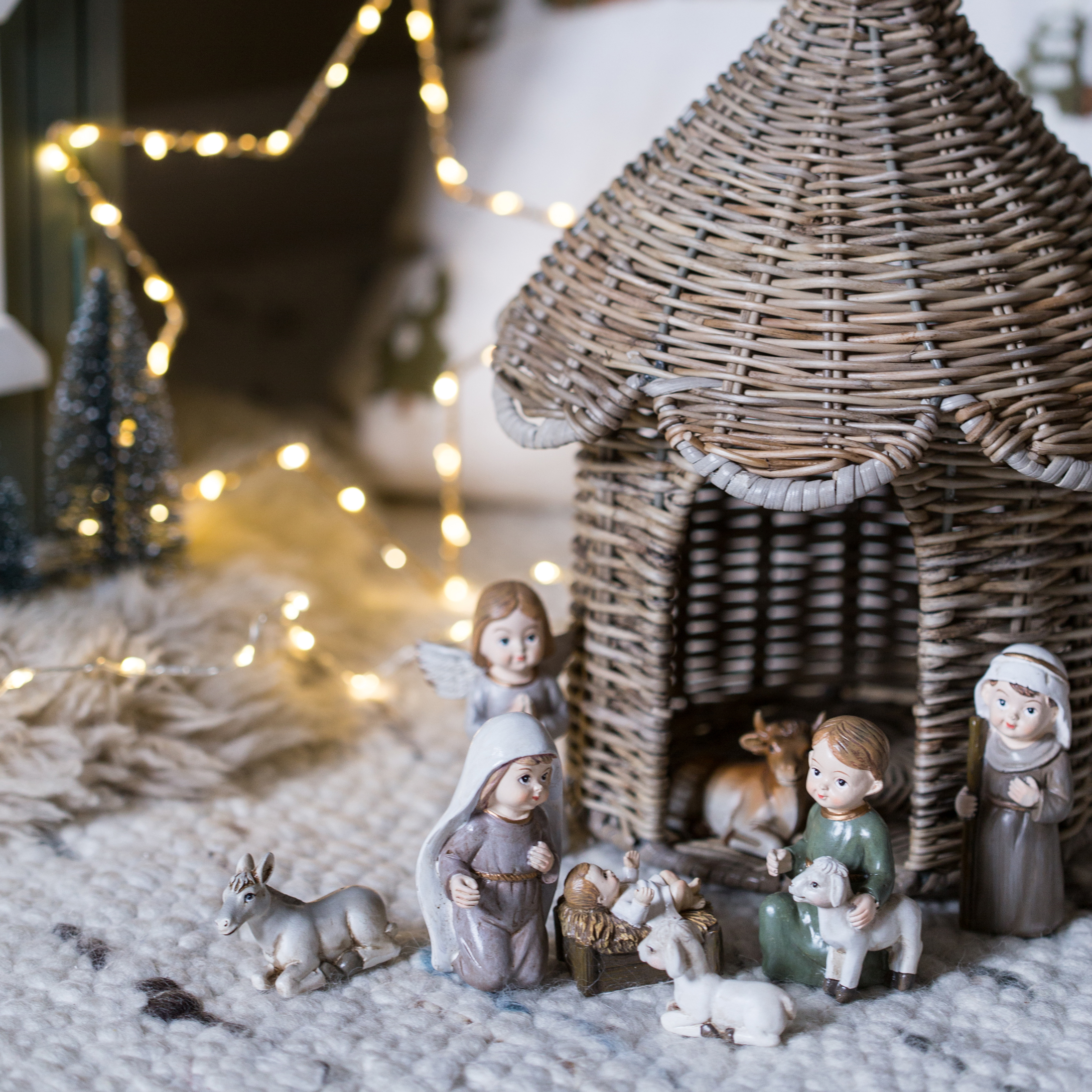 Figurines de crèche de Noël avec maison en osier et personnages sur tapis doux éclairé par guirlande lumineuse