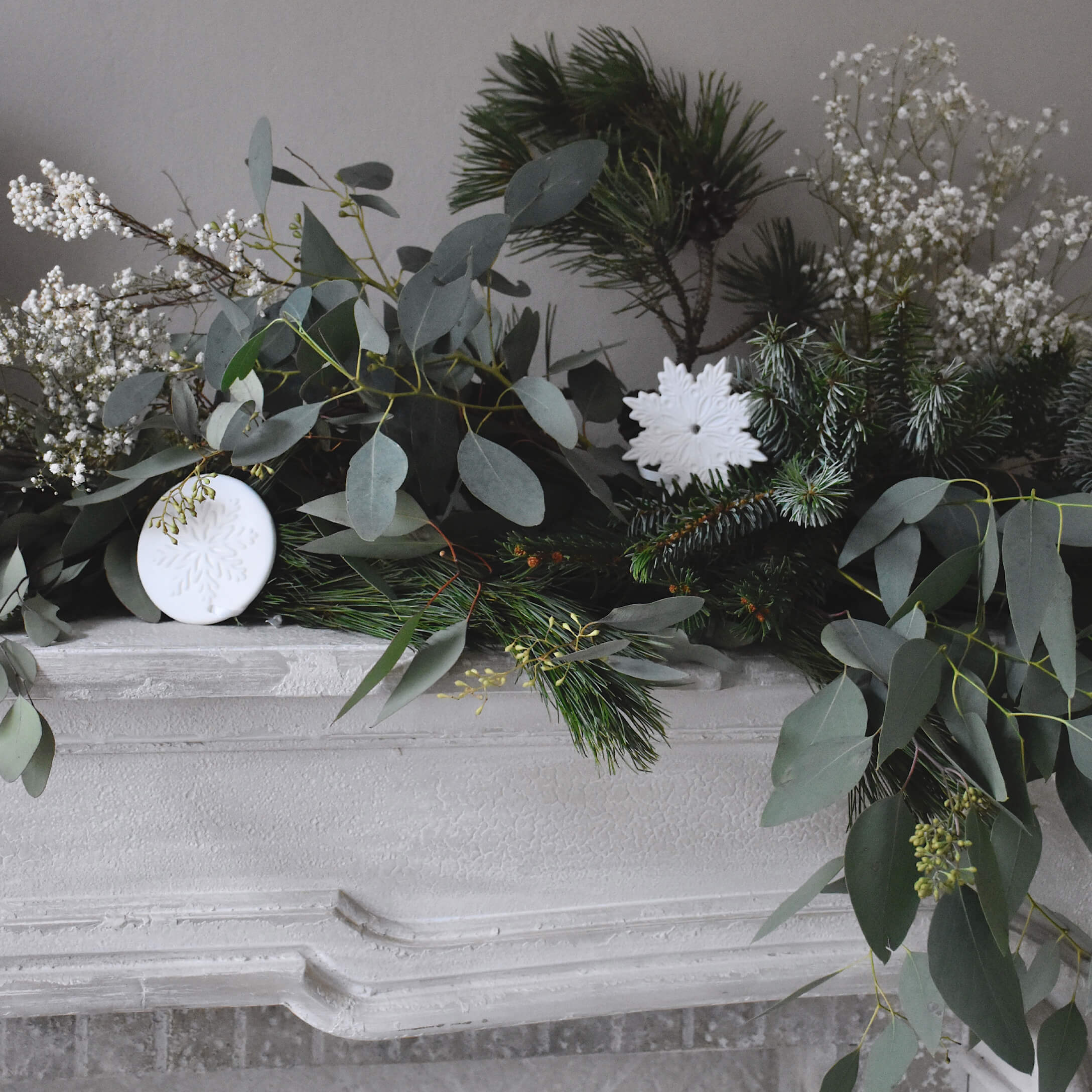 Couronne décorative en branches vertes et ornements blancs en forme de flocons sur une cheminée en pierre blanche