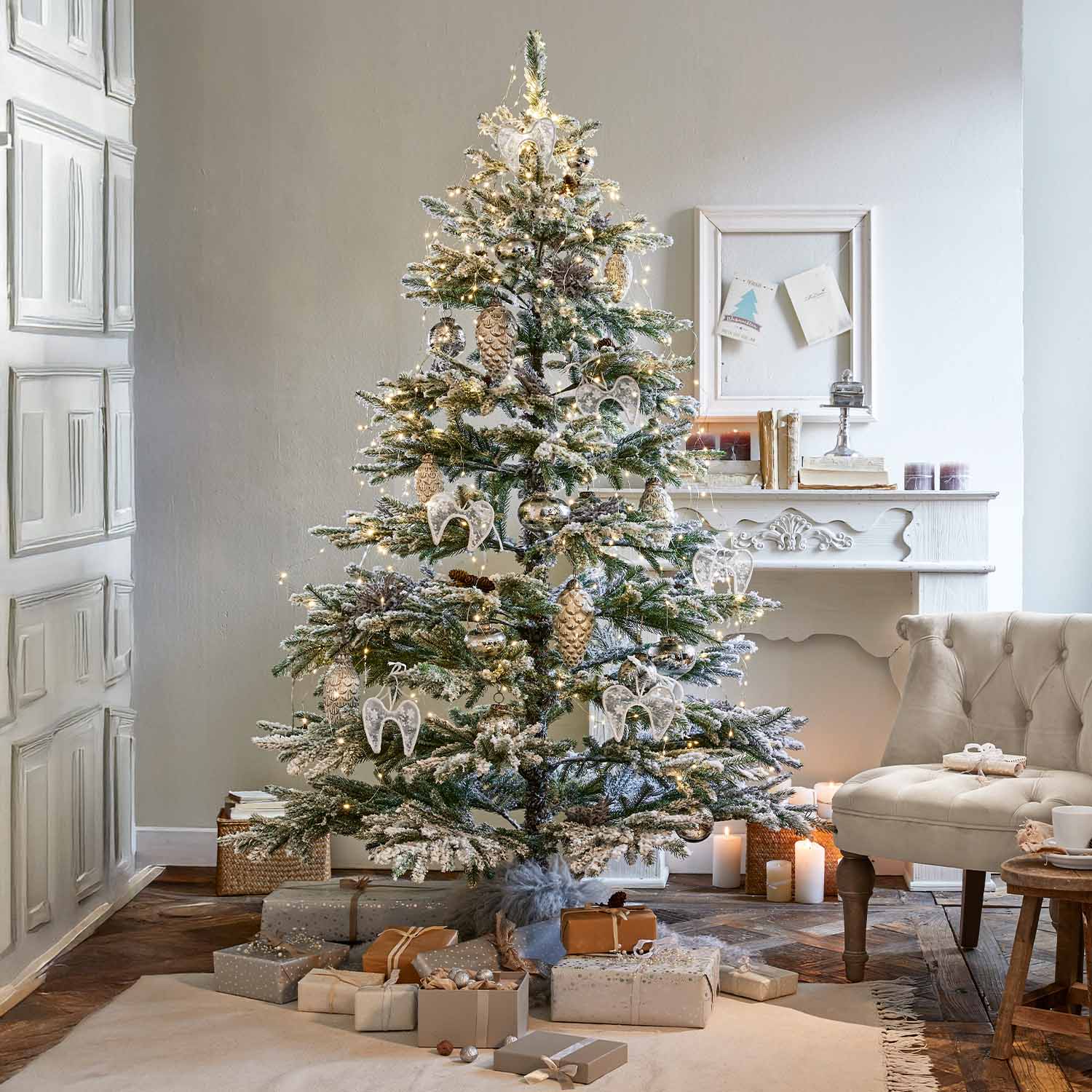 Sapin de Noël enneigé décoré d'anges blancs et de pommes de pin dorées avec cadeaux au pied dans un salon cosy