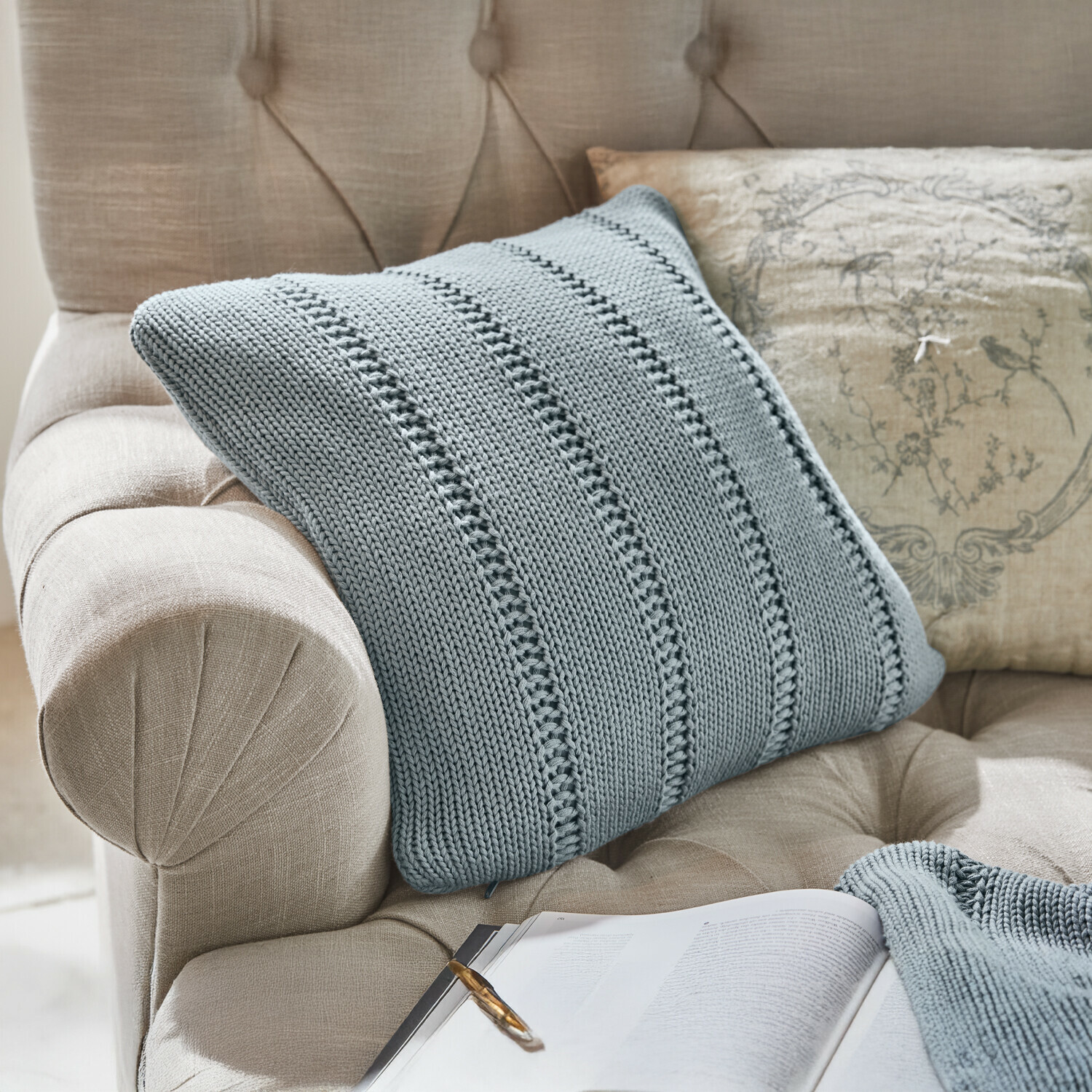 Fauteuil beige en tissu capitonné avec couverture tricotée grise et coussin décoratif