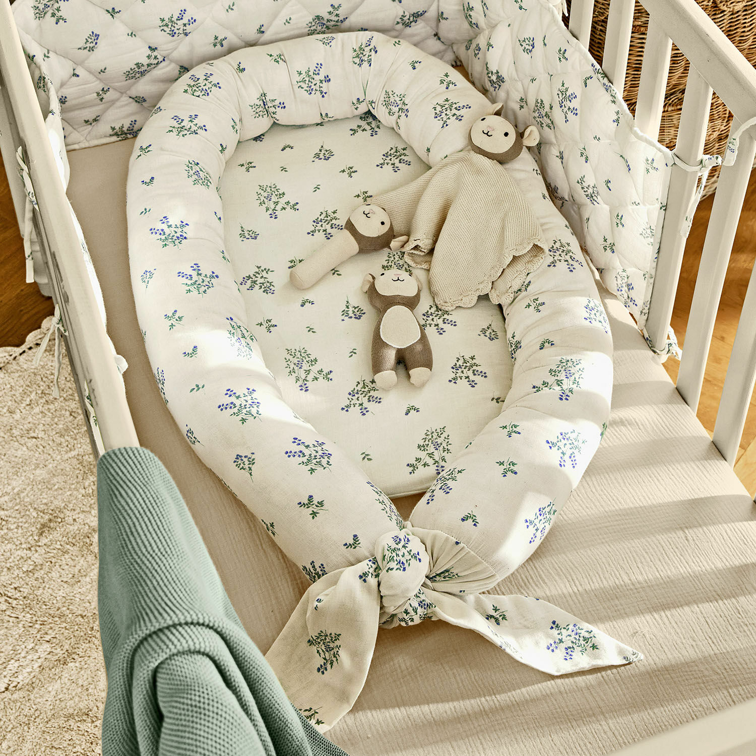 Tour de lit pour bébé Nymariel Nid d'ange blanc en coton avec motif floral bleu-vert et peluches dans un lit bébé en bois clair