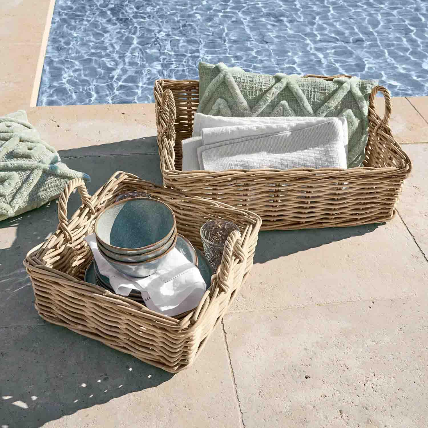 Deux paniers en osier avec poignées, garnis de coussins verts et serviettes blanches, au bord de la piscine