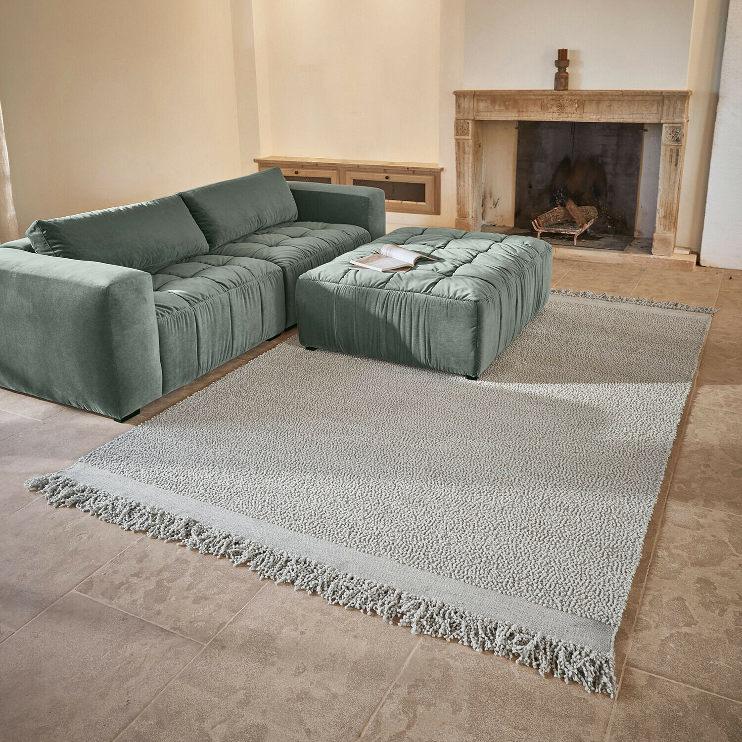 Vloerkleed Linnet Groene fluwelen bank met doorgestikte zitting en bijpassende poef op lichte vloerkleed bij open haard