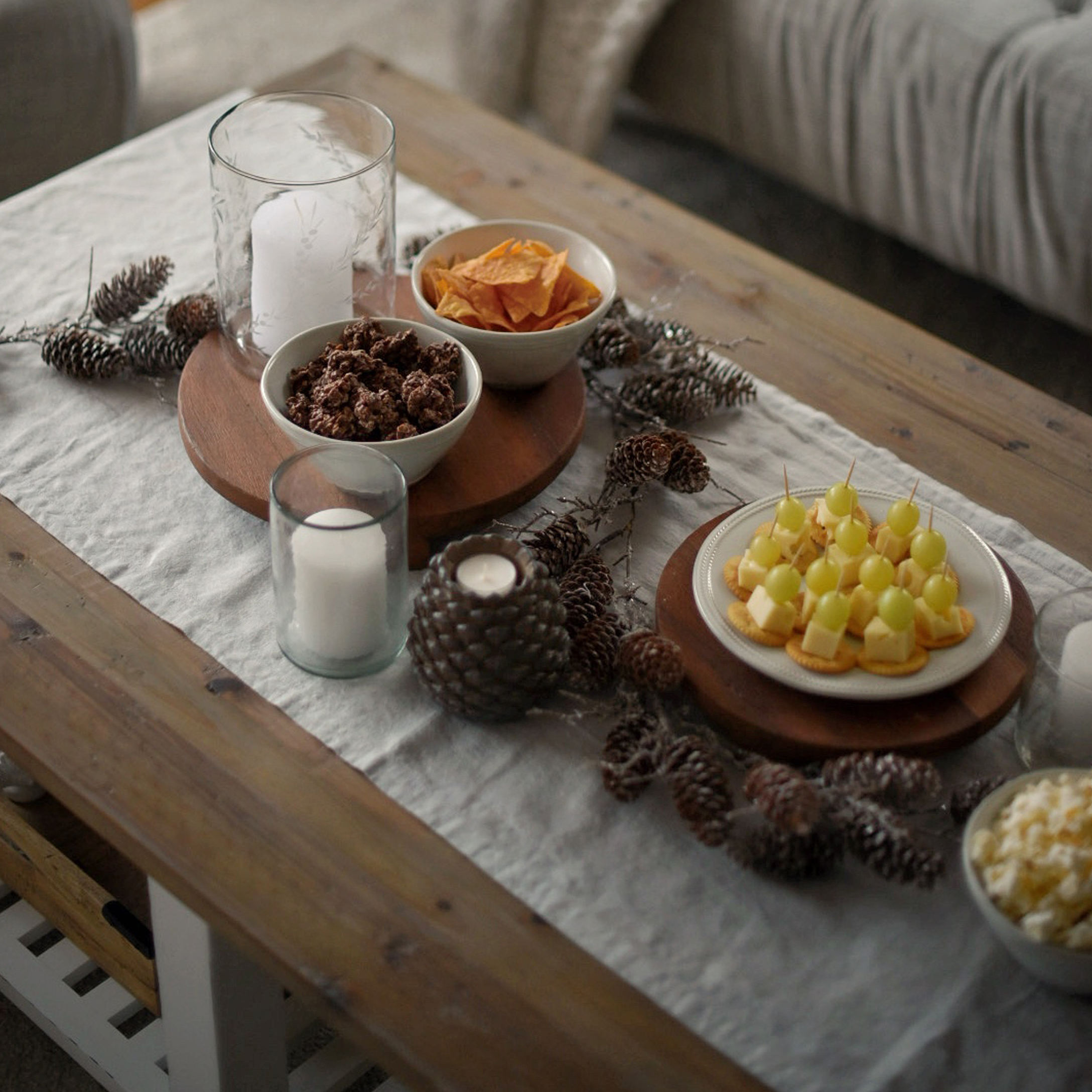Plateau en bois avec snacks et bougies sur une nappe en lin décorée de pommes de pin