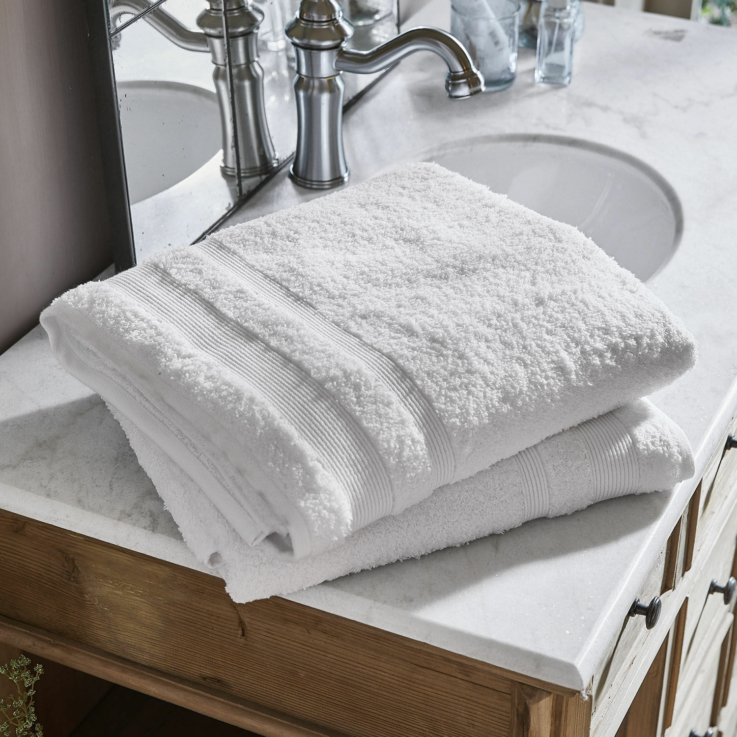 Lot de 2 draps de bain Bourogne Serviettes blanches en coton pliées sur un lavabo en marbre avec meuble en bois dans la salle de bain