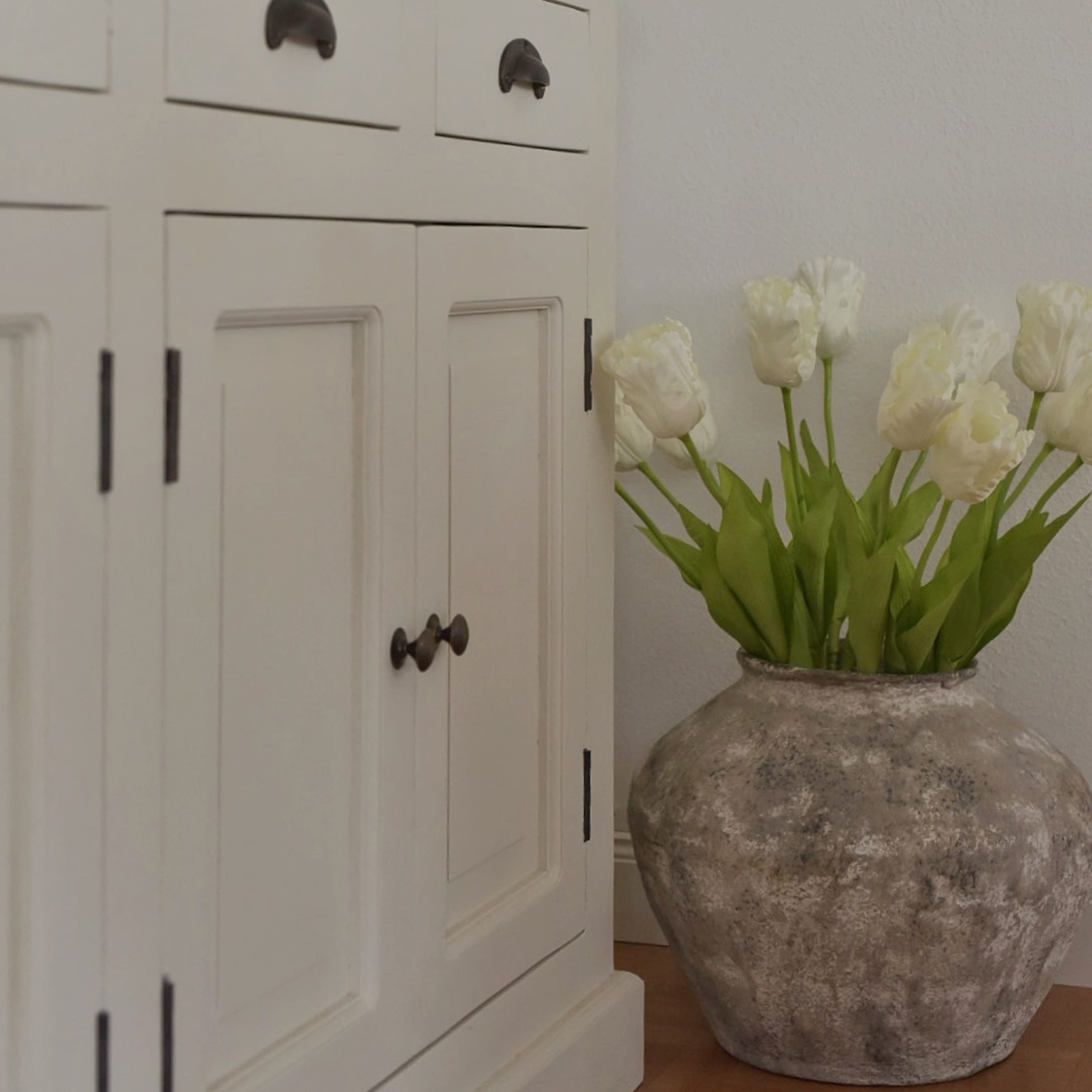 Grand vase en céramique grise avec tulipes blanches à côté d'un buffet en bois blanc