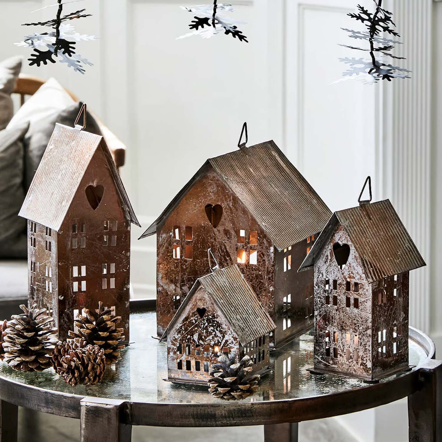 Maisons décoratives en métal avec cœurs découpés et fenêtres sur table en verre avec pommes de pin