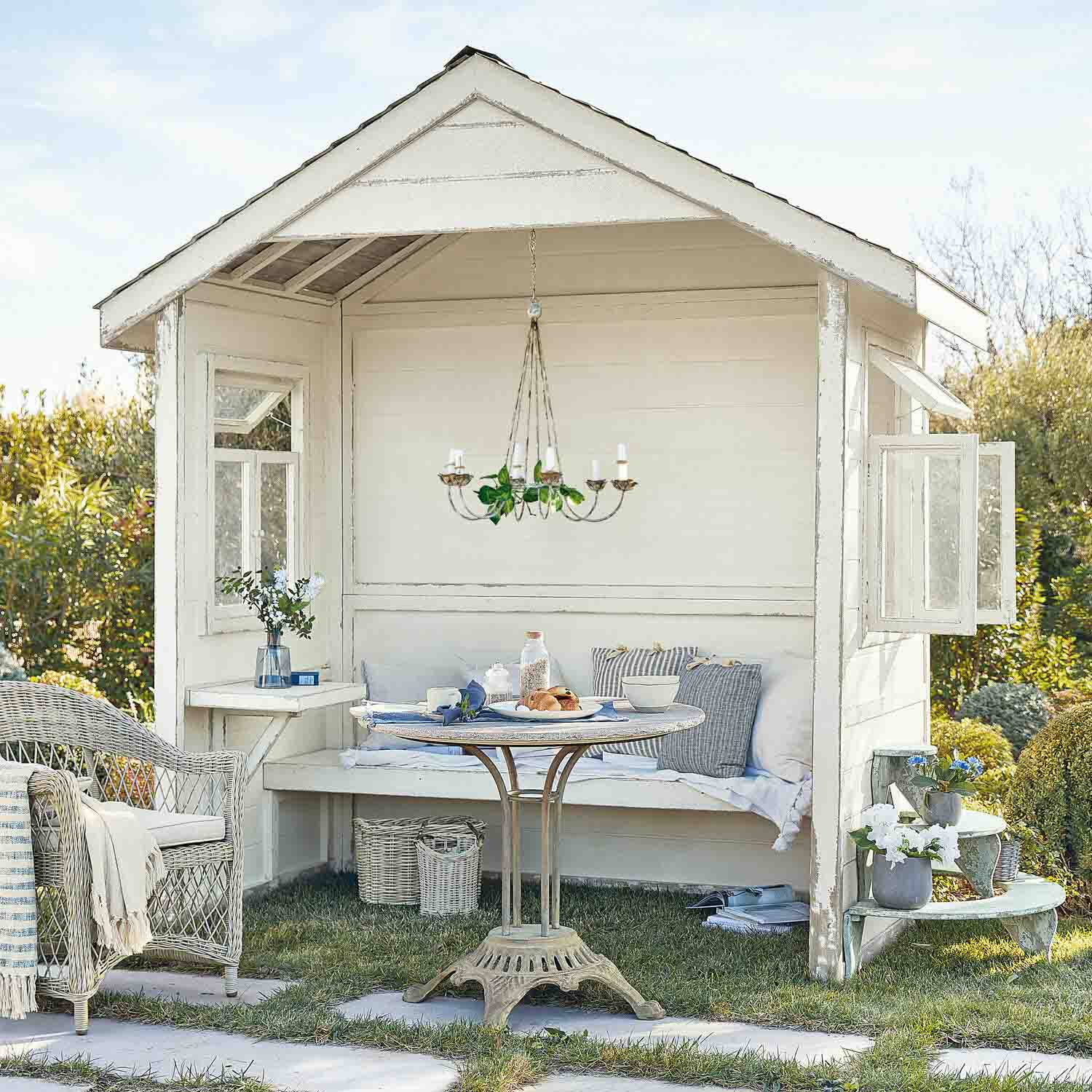 Kiosque de jardin en bois blanc avec fauteuil en osier et table ronde sur pelouse