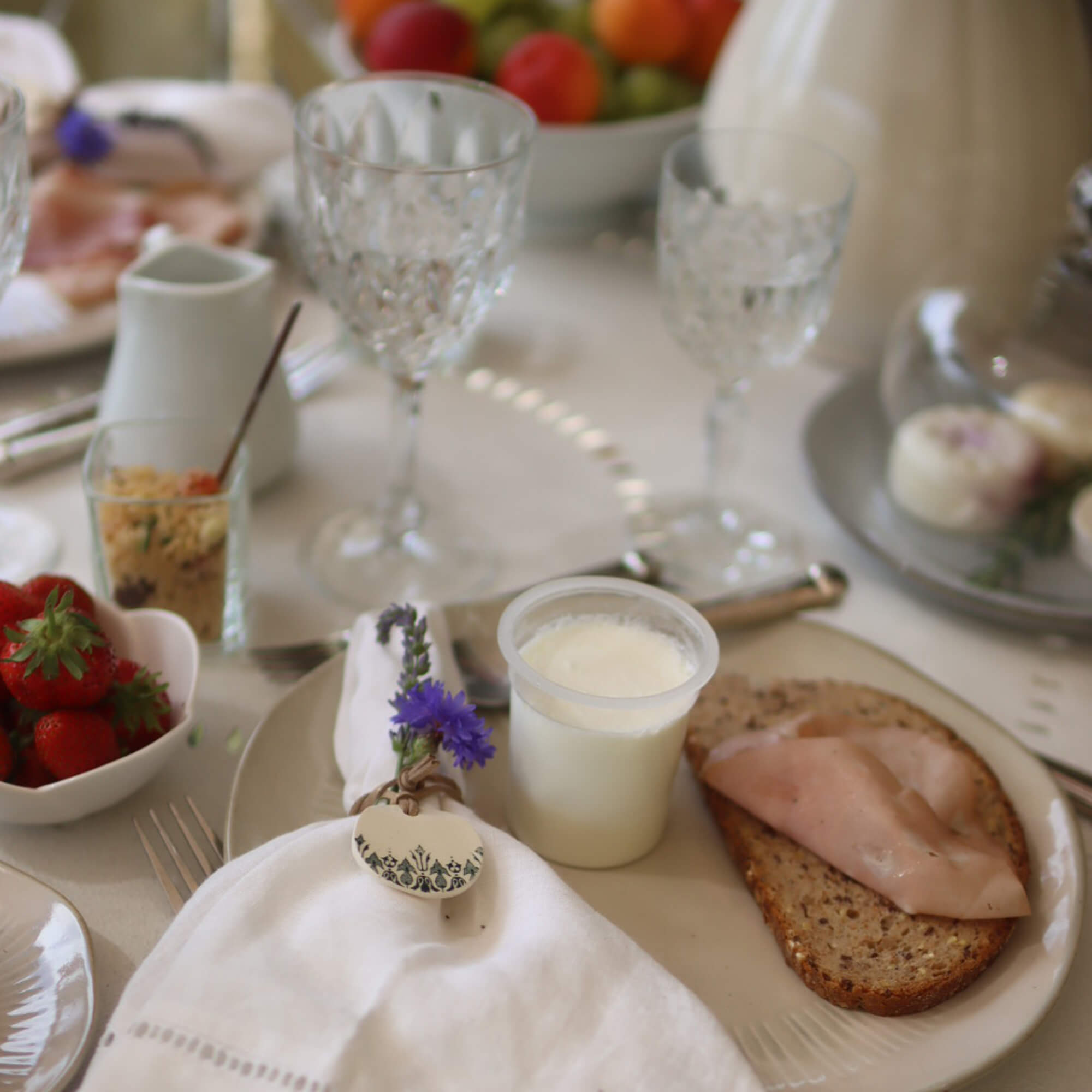 Table de petit-déjeuner avec pain complet, jambon et yaourt sur assiette, serviette décorée de fleurs