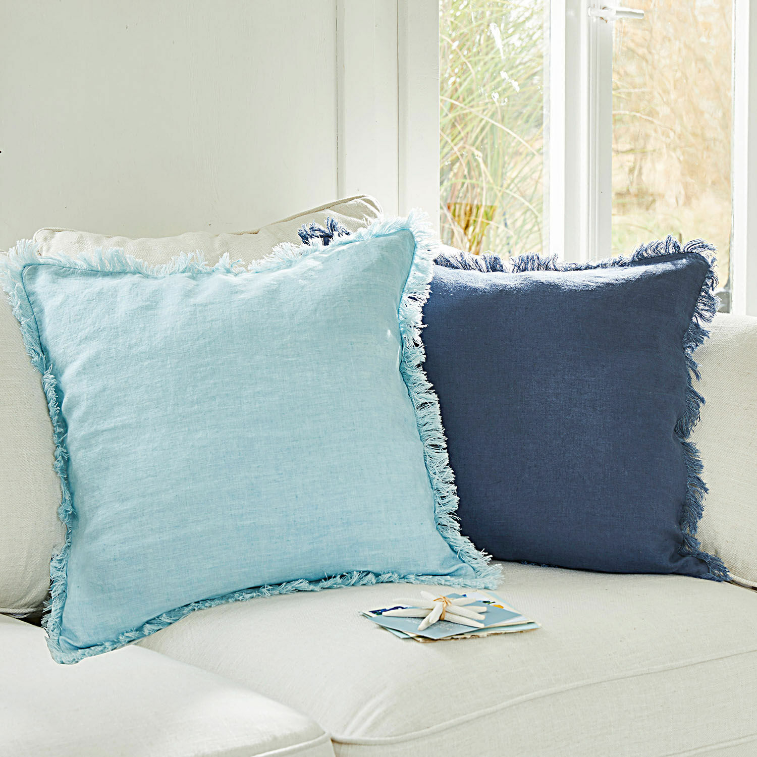 Lot de 2 housses de coussins Quebo Ensemble de deux coussins décoratifs en lin bleu clair et bleu marine avec franges sur un canapé beige