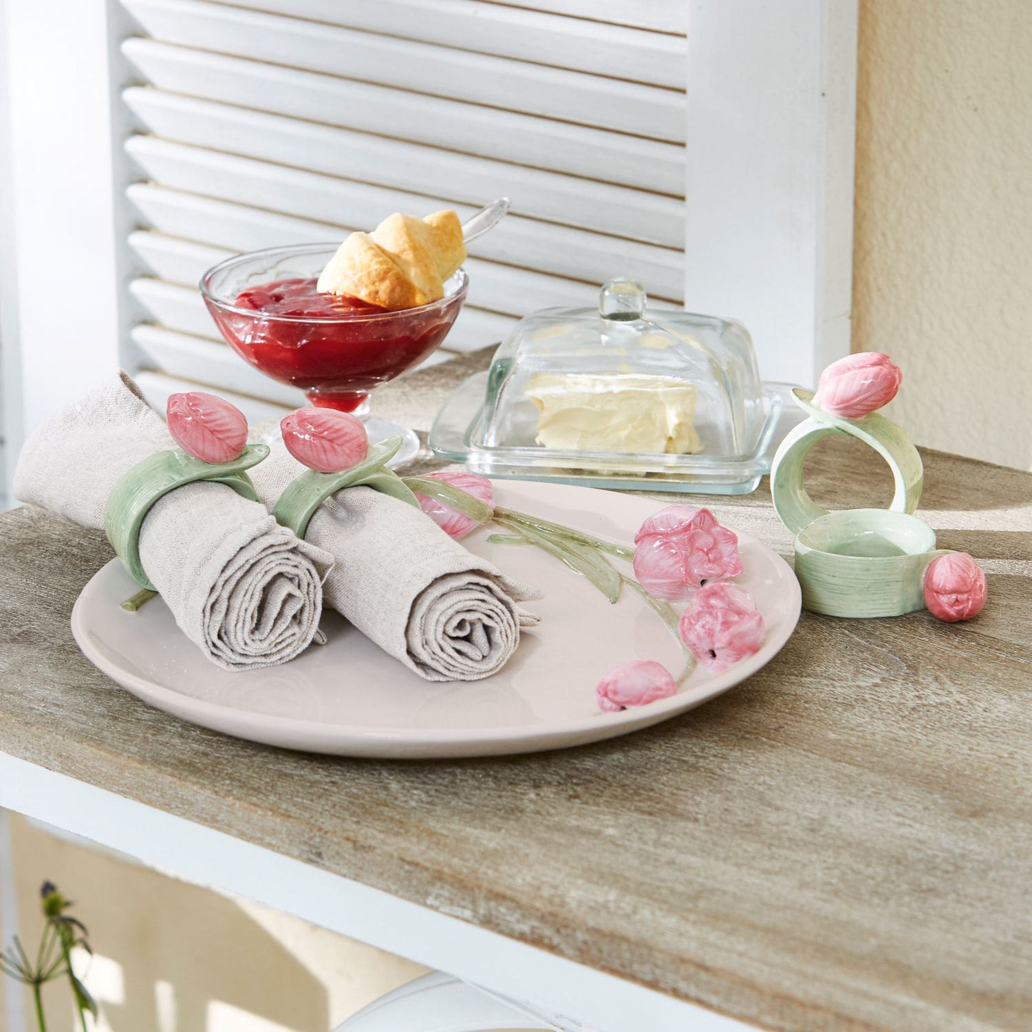 Lot de 4 ronds de serviettes Monique Ronds de serviette en céramique avec fleurs roses sur assiette beige posée sur table en bois