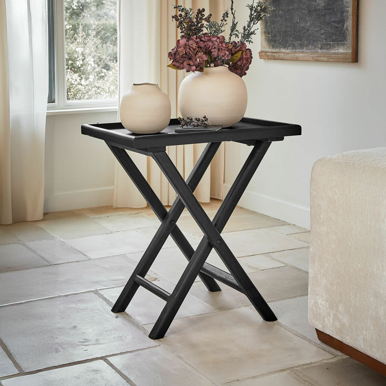Table d’appoint Paventino Table pliante noire en bois avec deux vases beiges et décoration florale dans un salon lumineux