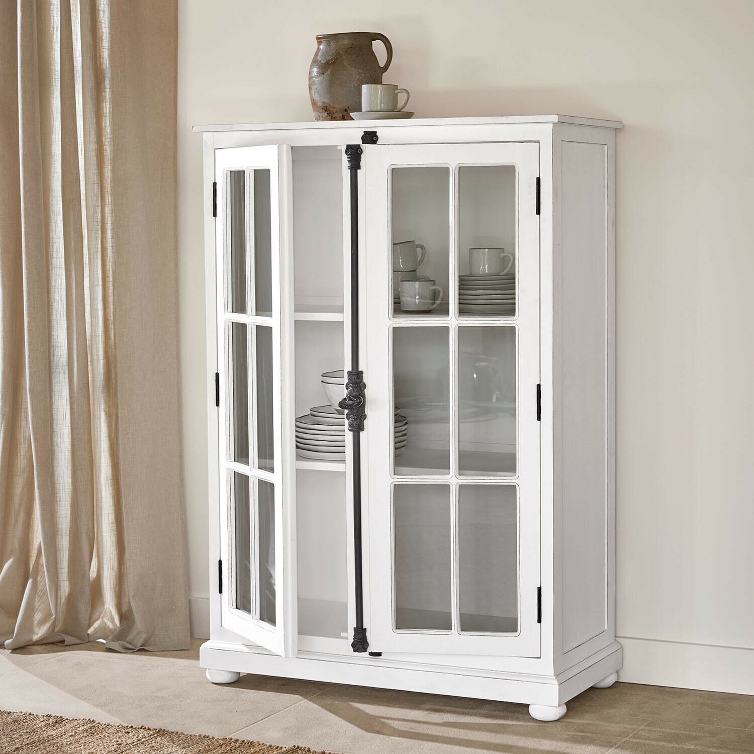 Vitrine Salivonne Vitrine en bois blanc avec portes vitrées et poignées en métal noir style vintage dans un intérieur clair