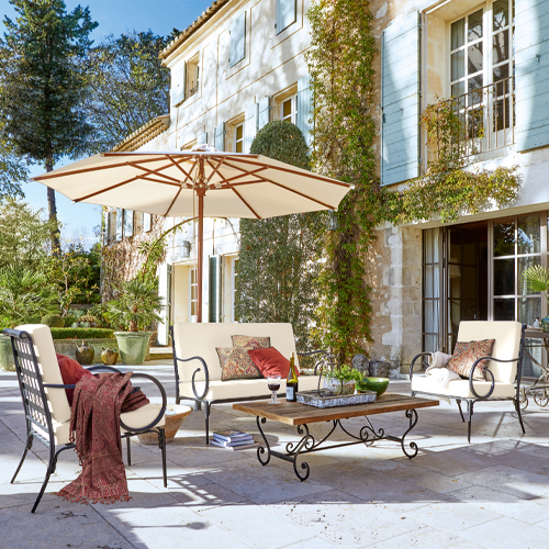 Tuinmeubelset met metalen frames en crèmekleurige kussens op stenen terras met parasol