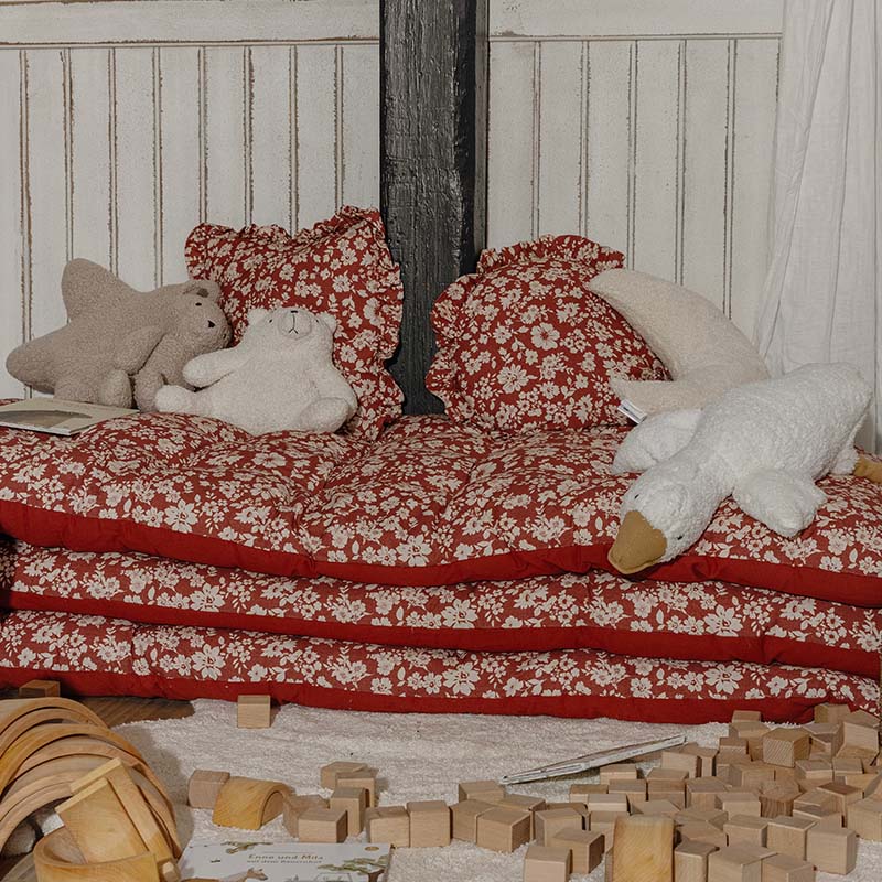 Coussins et matelas rouges à fleurs avec peluches sur un coin enfant entouré de blocs de bois pour jouer