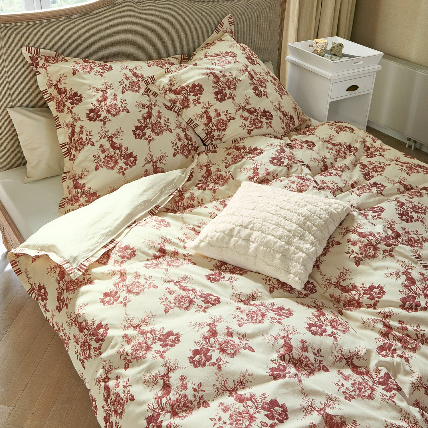 Dekbedovertrekset Renique Katoenen beddengoed in crème met rood hert- en bloemenpatroon, decoratief kussen op bed