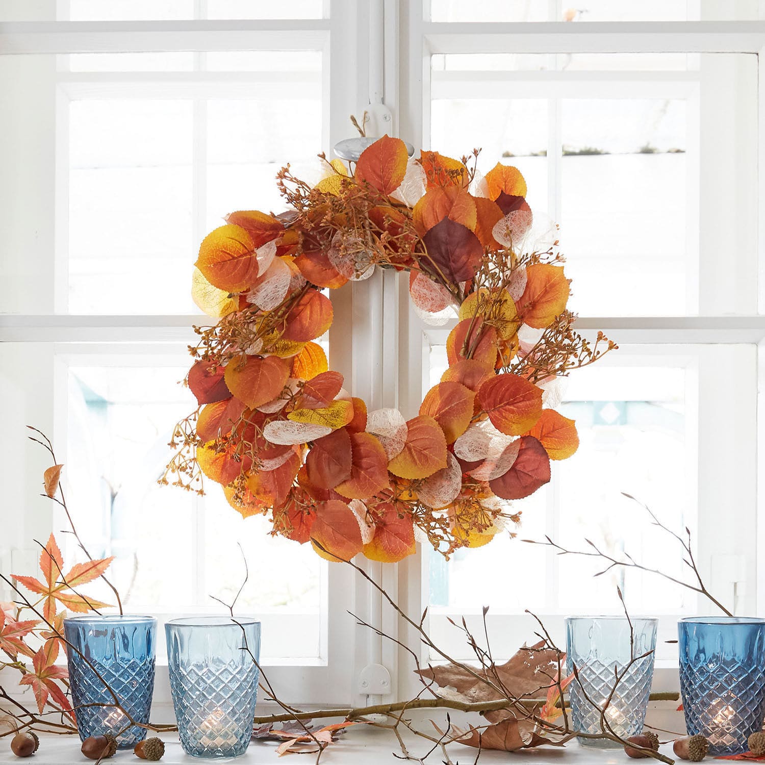 Herfstkrans met oranje en gele bladeren aan wit raam, seizoensdecoratie