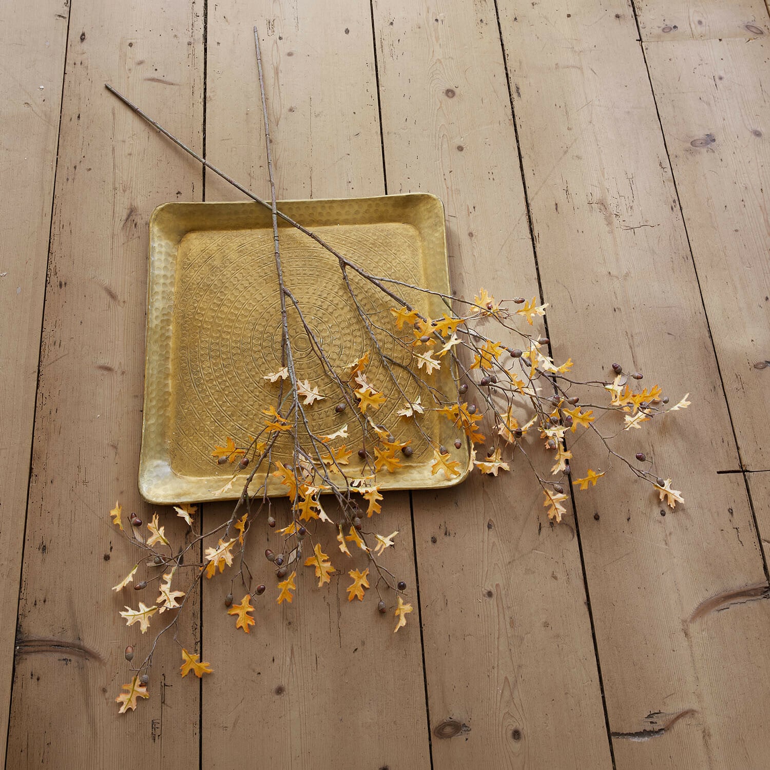 Lot de 2 tiges décoratives Sagges Plateau carré en laiton martelé avec branches décoratives aux feuilles jaunes sur un sol en bois