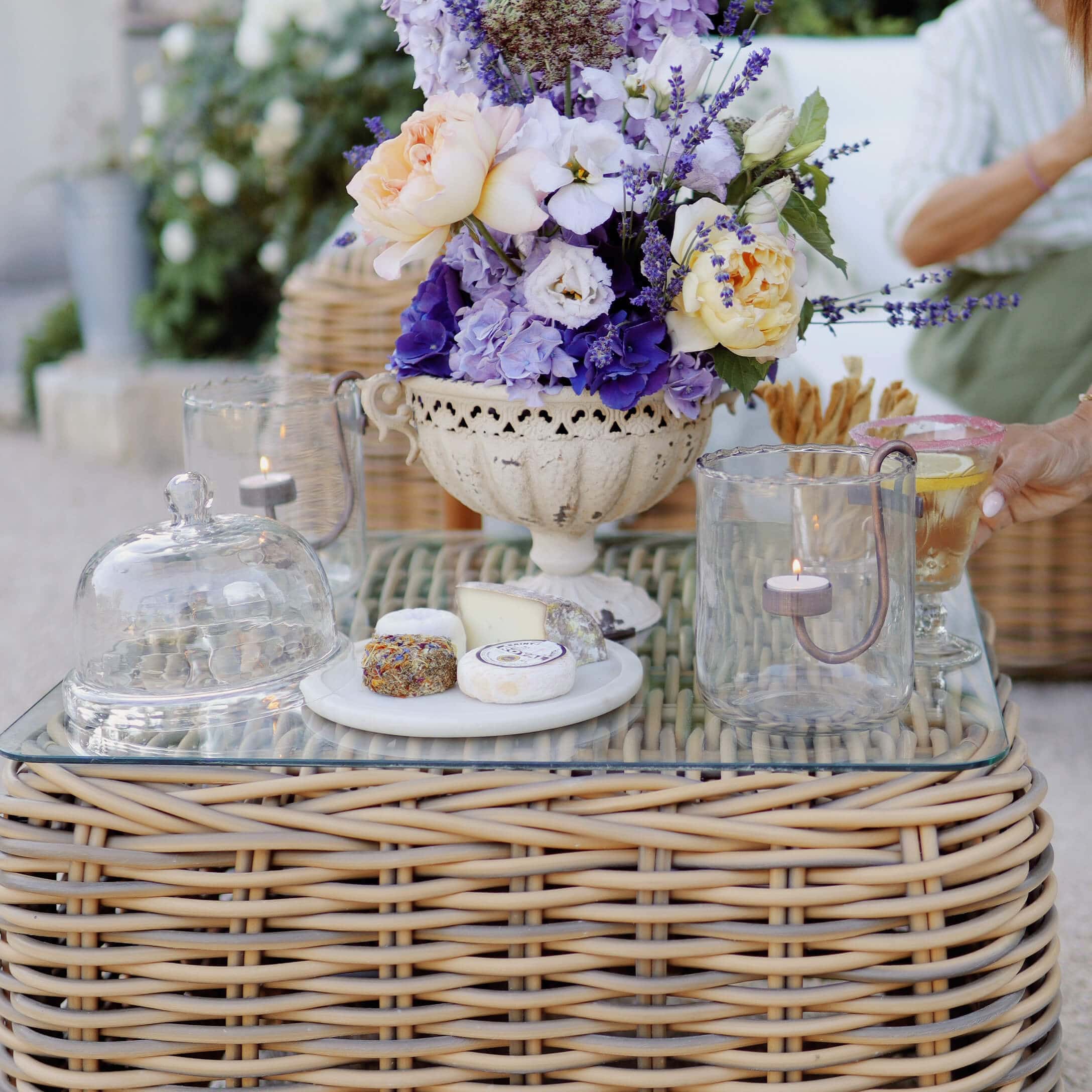 Bouquet décoratif de lavande et roses dans un vase en céramique blanche sur table en rotin avec verre