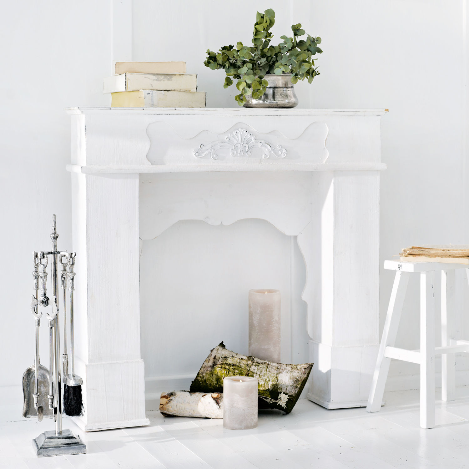 Haardschouw Margaux Witte houten schoorsteenmantel met decoratief reliëf, kaarsen en metalen haardgereedschap