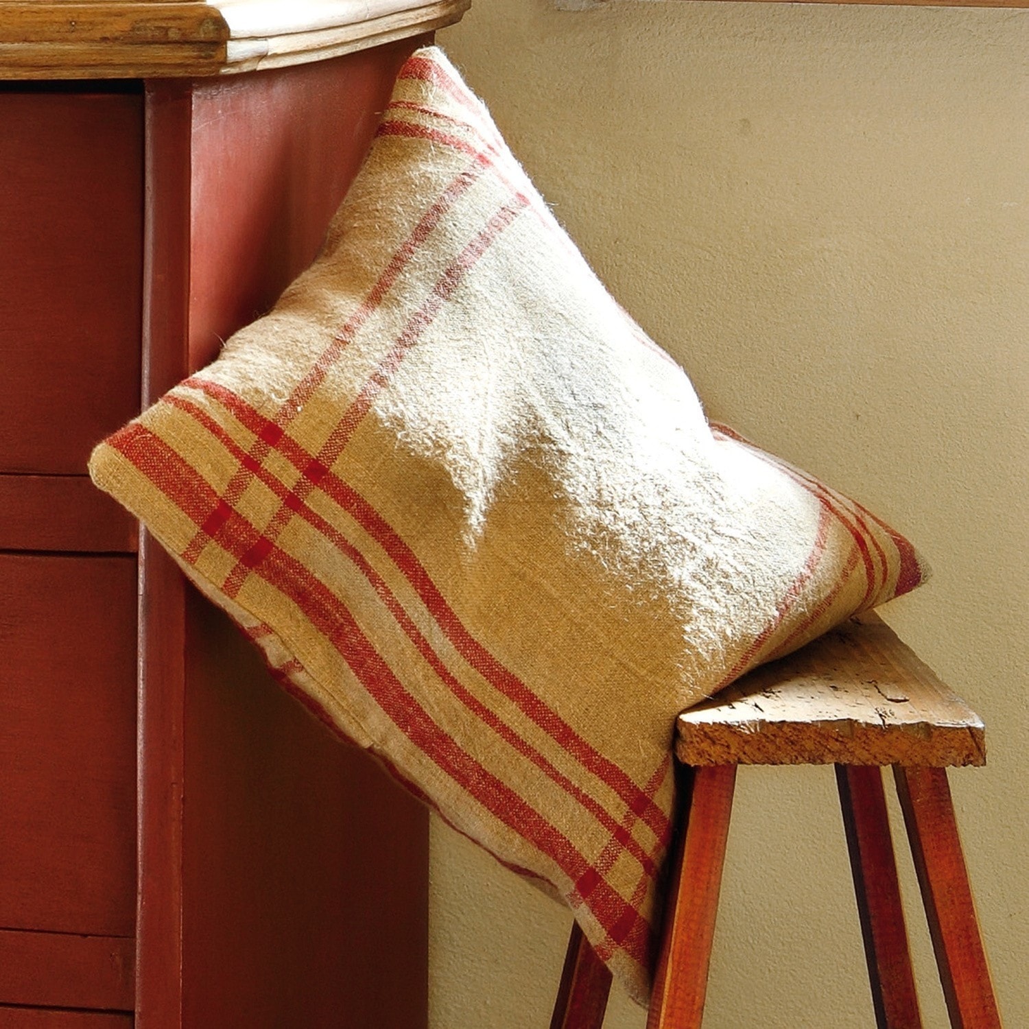 Beige kussen met rood ruitpatroon op houten bank, sfeervolle interieurdecoratie