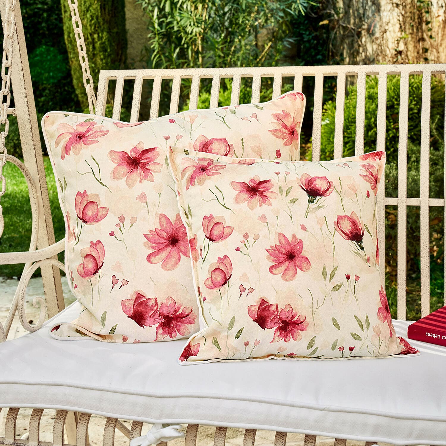 Twee decoratieve kussens met bloemenpatroon op een witte tuinschommel, katoen, lichtroze bloemen