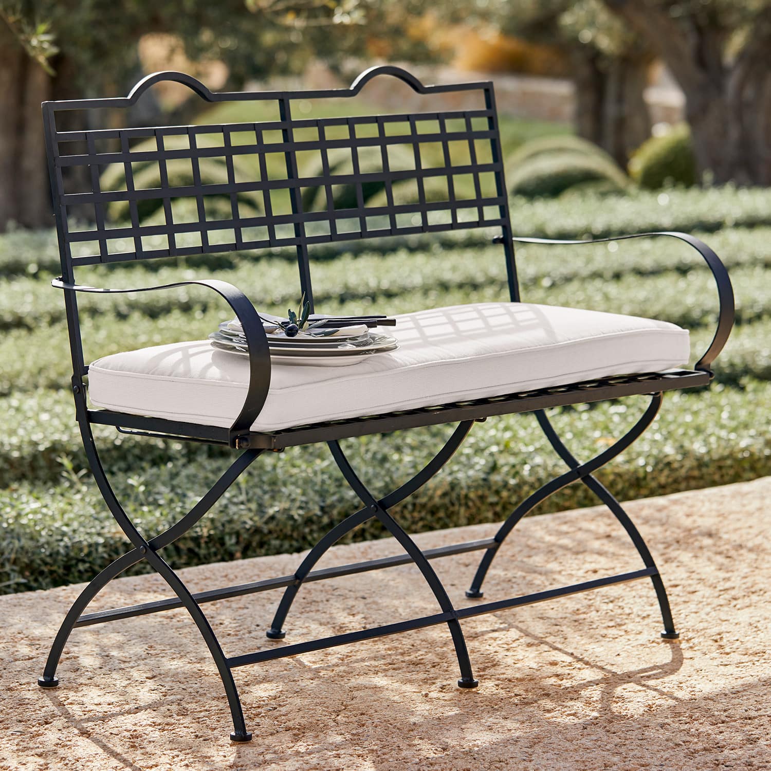 Banc de jardin en métal noir avec coussin blanc sur terrasse en pierre ensoleillée