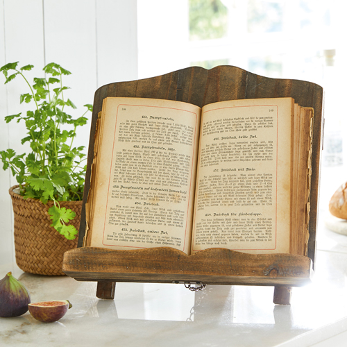 Support à livre de cuisine en bois naturel sur un plan de travail clair avec plante et figues
