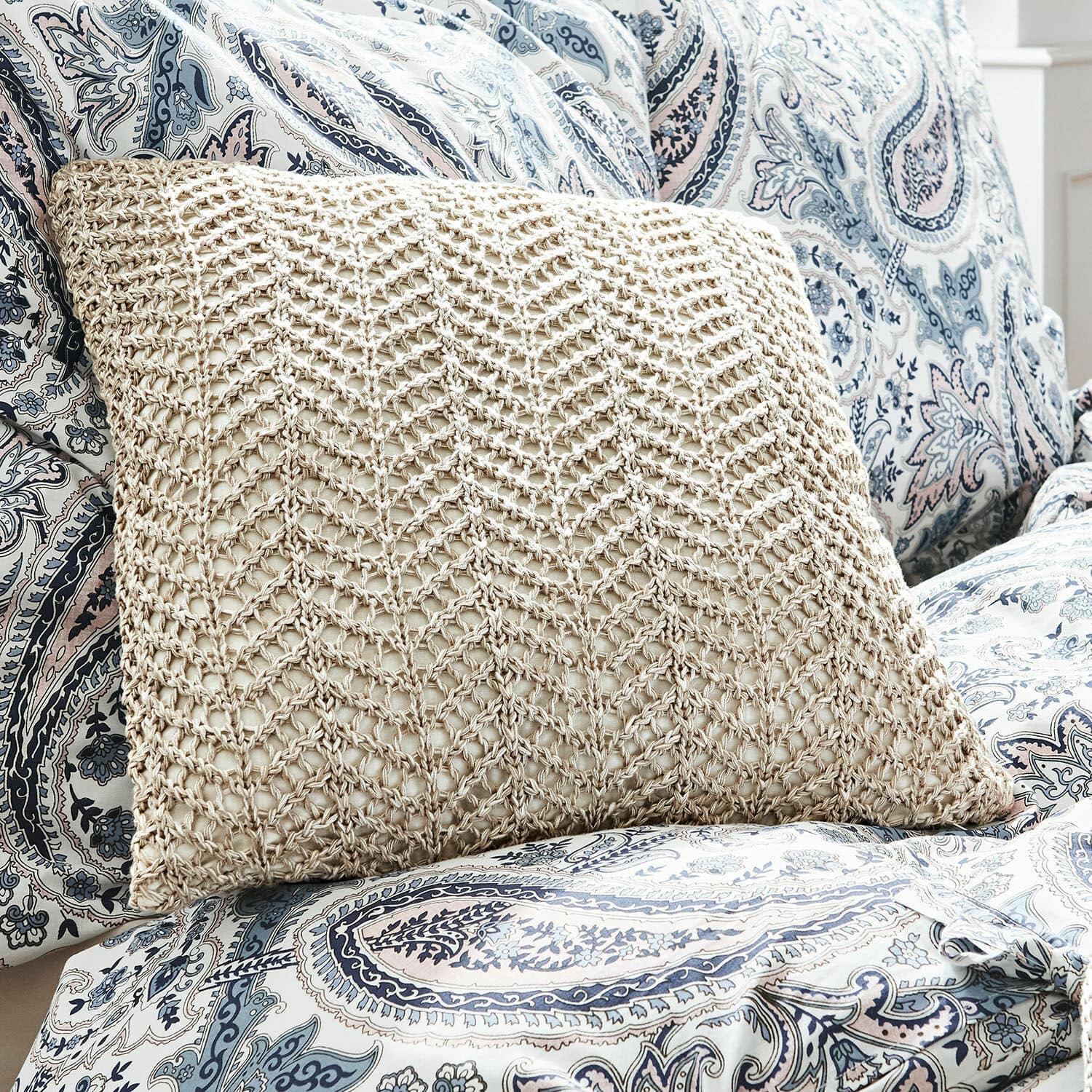 Beige kussen met gevlochten patroon op blauw-witte paisley hoes