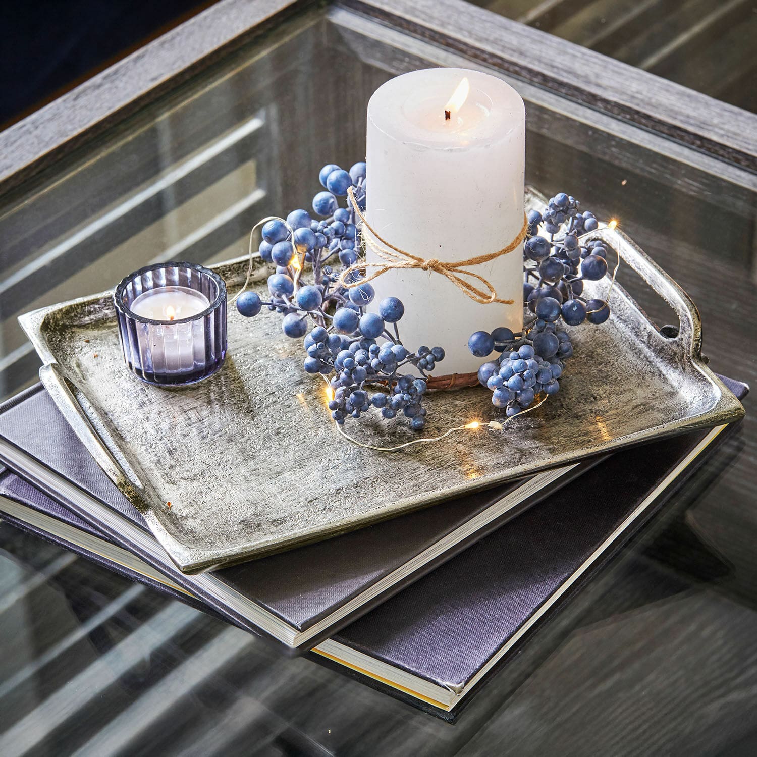 Lot de 2 plateaux Branora Bougie blanche avec corde naturelle et décor de baies bleues sur plateau en métal posé sur table en verre