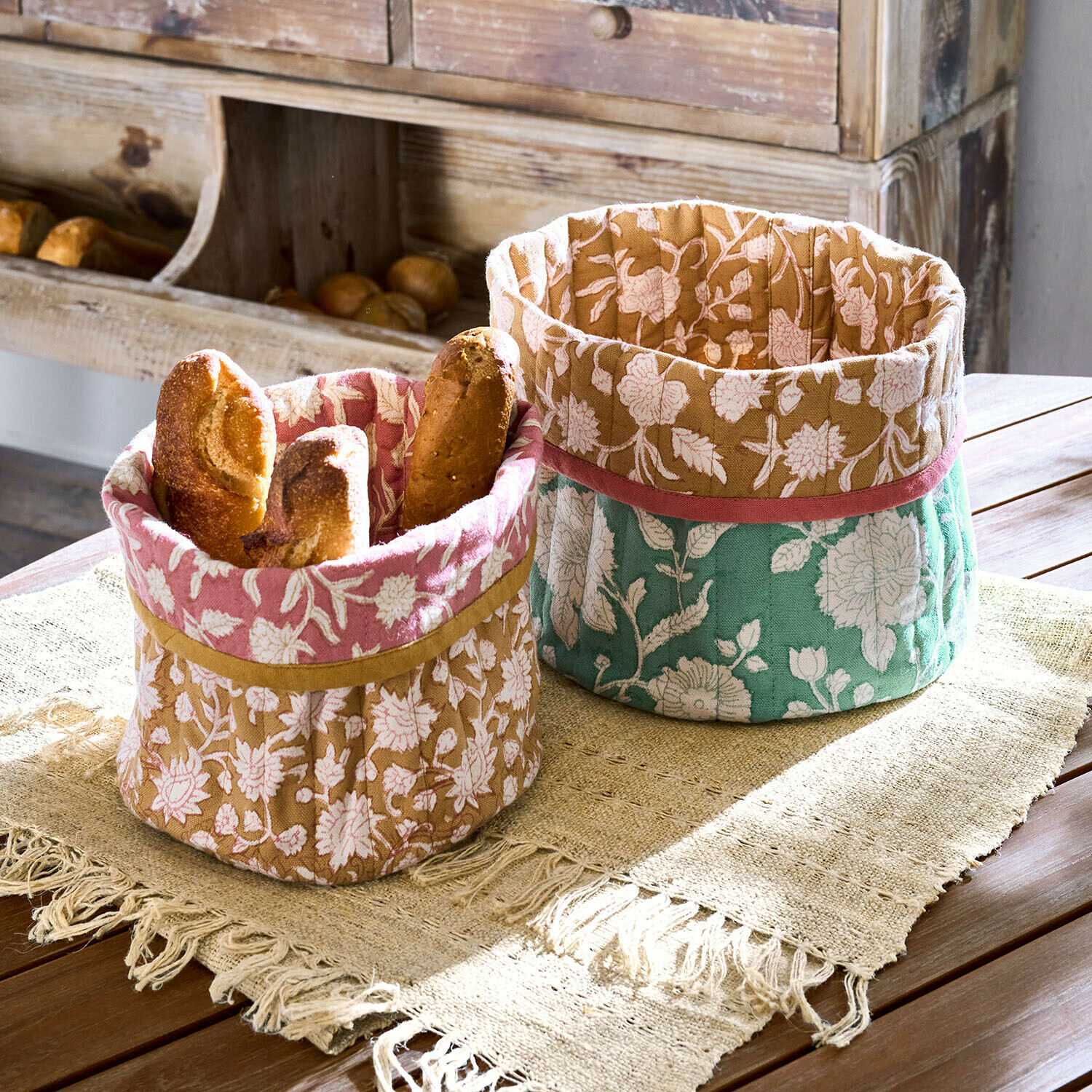 Mand set van 2 Fleuronnes Twee decoratieve katoenen manden met bloemmotief in roze, bruin en groen voor brood op houten tafel