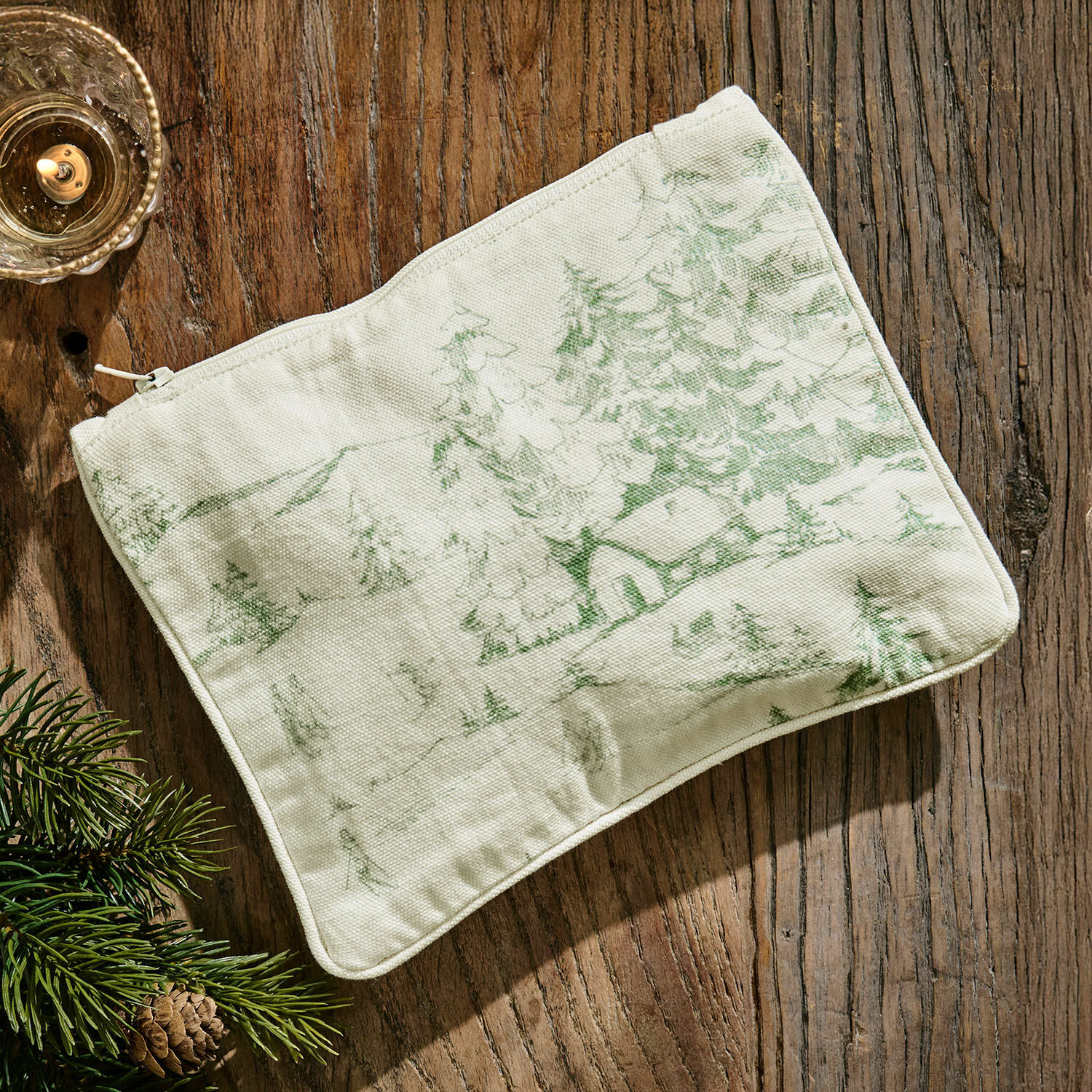 Pochette Norathia Trousse beige en coton avec imprimé vert de paysage forestier posée sur une table en bois