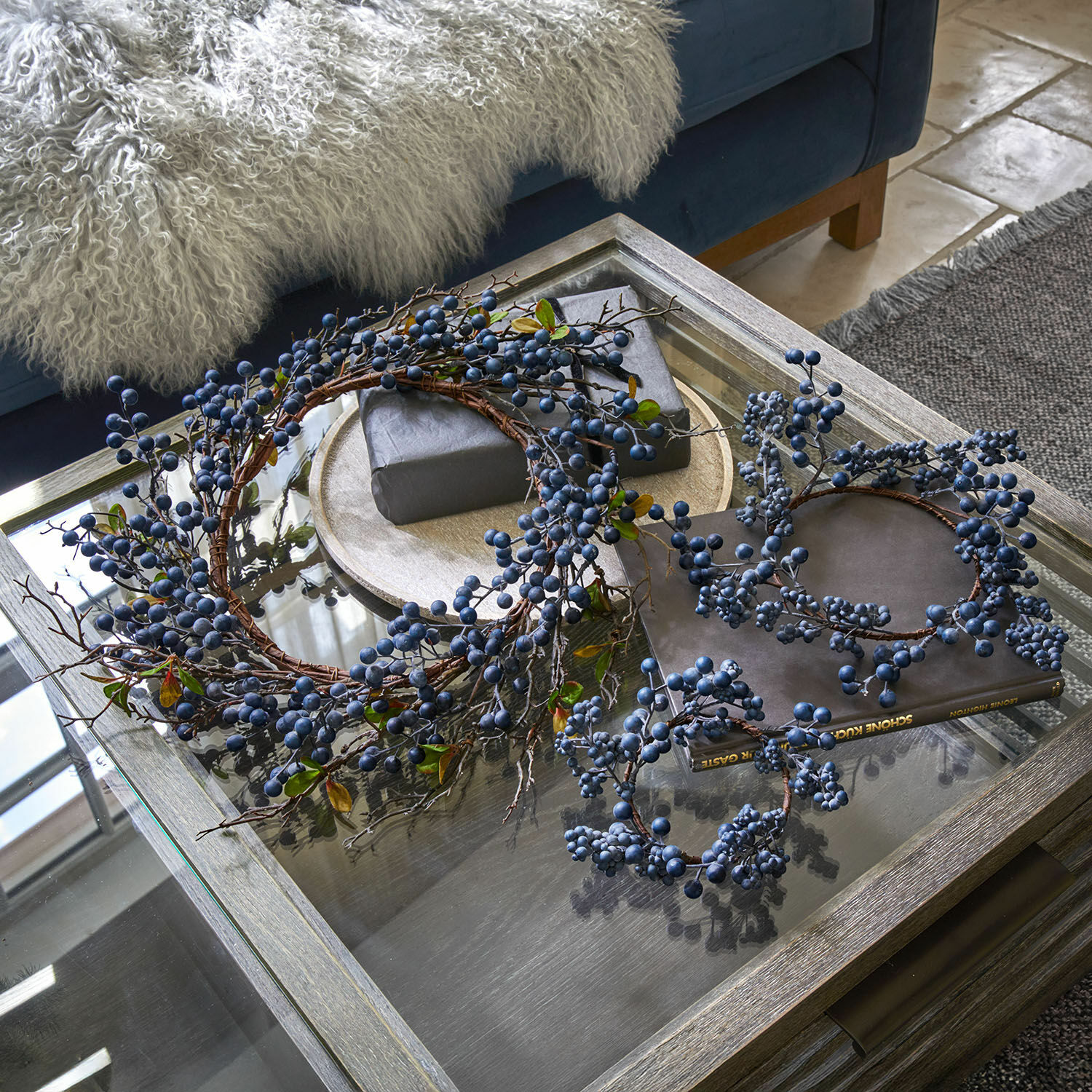 Lot de 3 couronnes Kireen Couronnes décoratives aux baies bleues sur une table en verre dans un salon avec plaid doux
