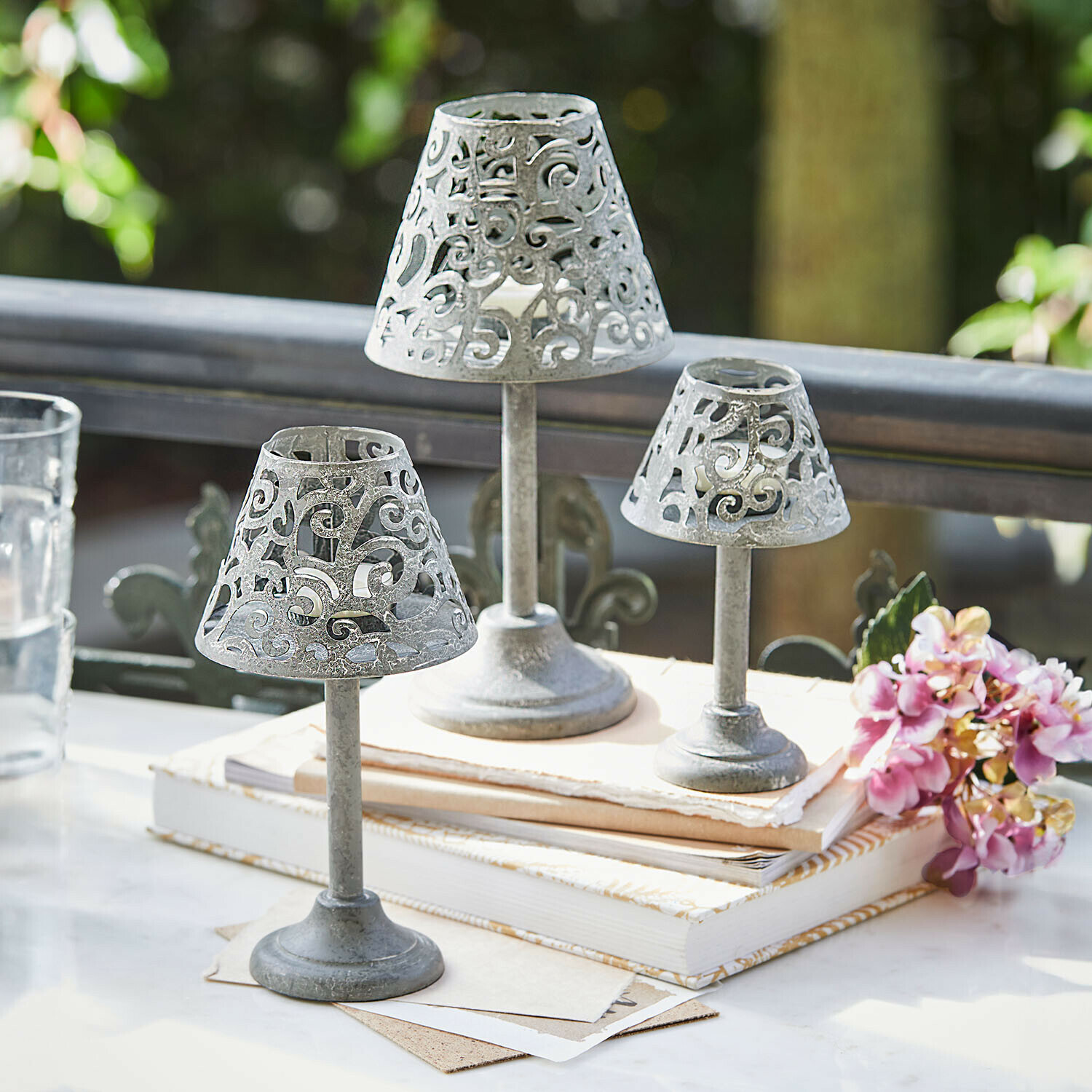 Lot de 3 photophores Belori Ensemble de trois bougeoirs en métal gris avec motif ajouré posés sur des livres sur une table