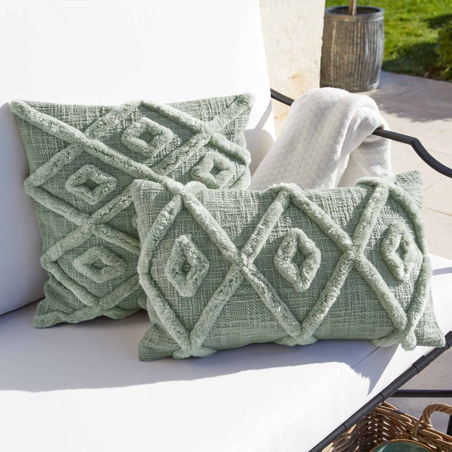 Coussin décoratif vert doux avec motif géométrique sur fauteuil blanc d'extérieur