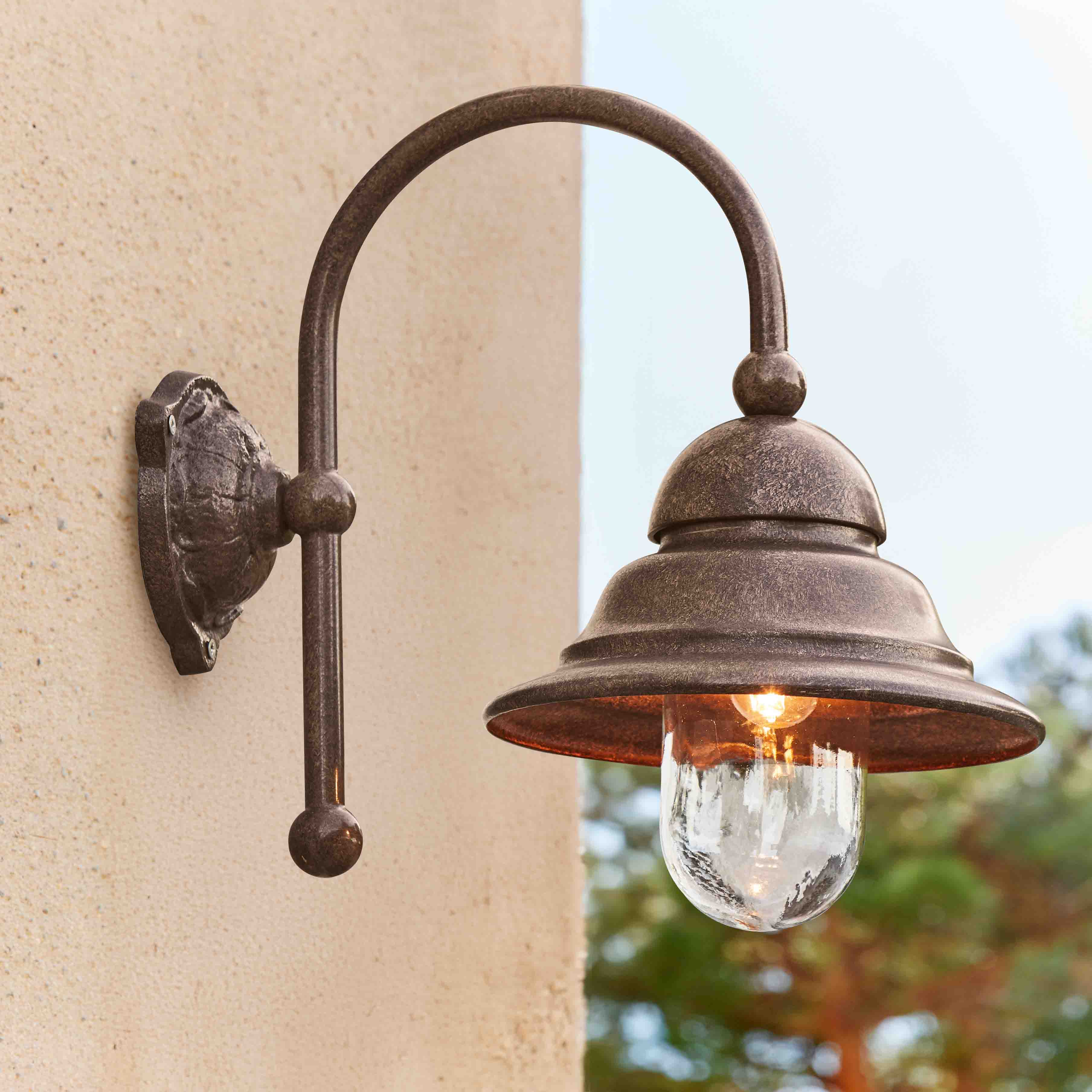 Buitenwandlamp van roestkleurig metaal met heldere glazen kap en warm LED-licht