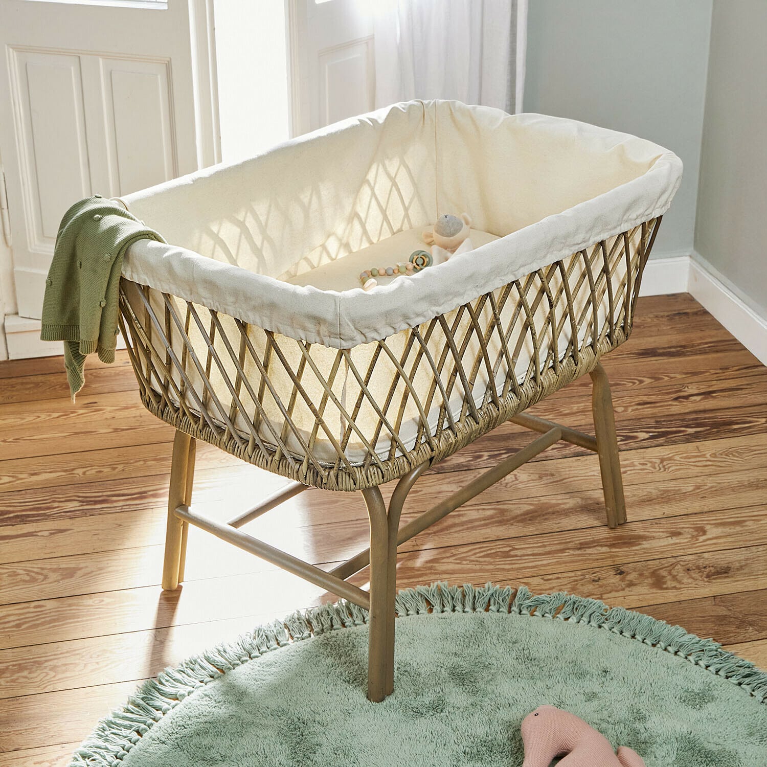 Berceau Nuvinas Berceau en osier avec doublure crème et couverture verte sur pieds en bois dans une chambre d'enfant