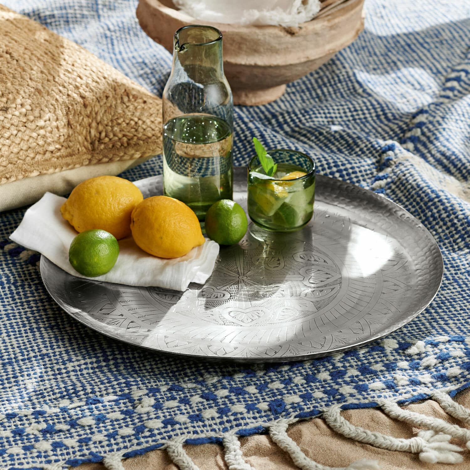 Plateau Moleur Plateau rond en métal gravé posé sur un plaid bleu et blanc avec citrons et citrons verts