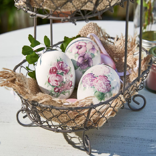 Drie witte keramische eieren met bloemenpatronen in metalen mand met jute op tafel