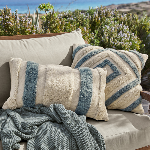 Coussins décoratifs beige et bleu en tissu doux sur canapé gris en extérieur, textiles pour jardin
