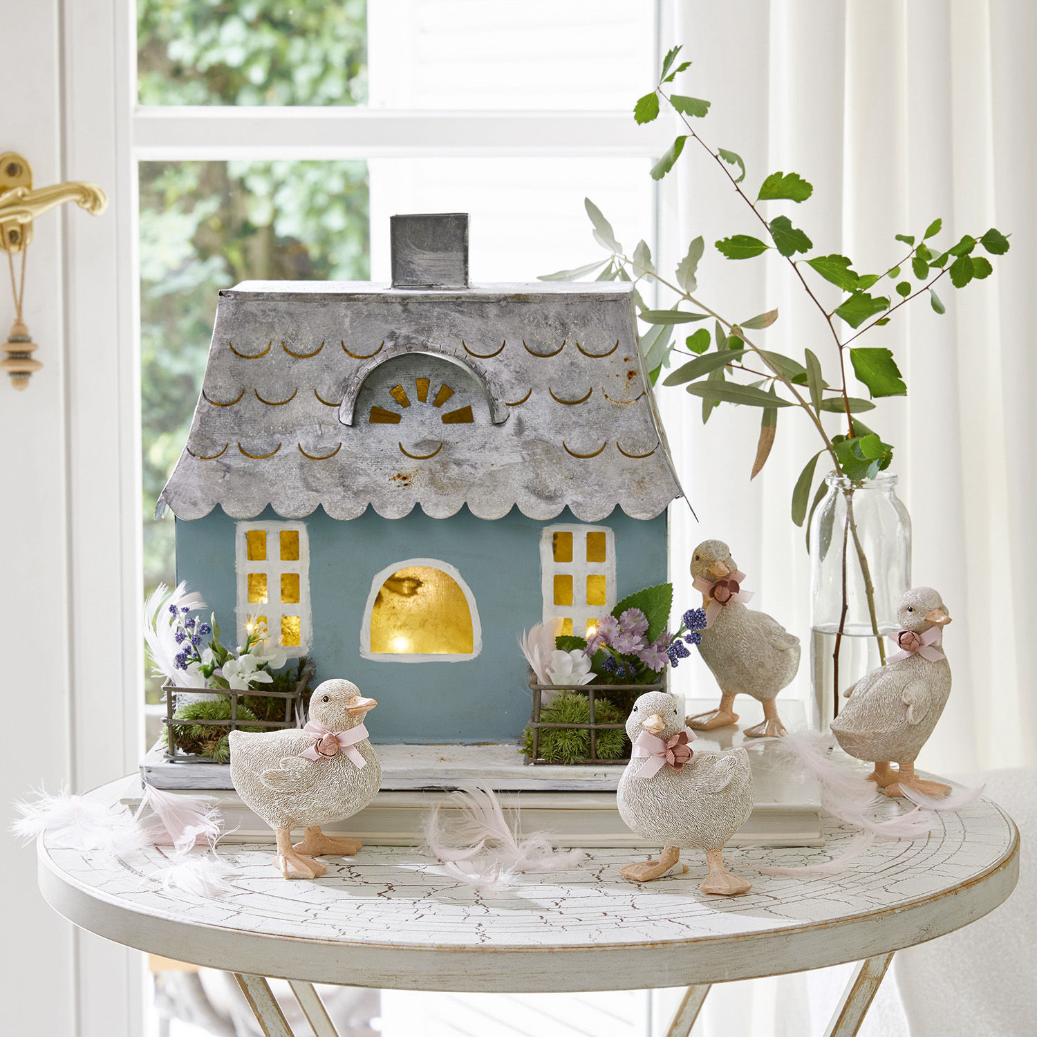 Petite maison décorative Nesrine Maison décorative en métal bleu avec quatre canetons blancs et fleurs sur une table ronde blanche