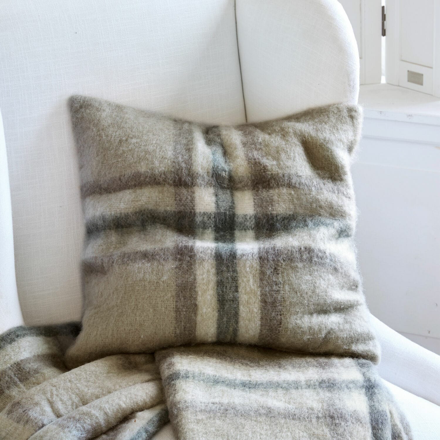 Housse de coussin Argoub Coussin et plaid en laine à carreaux beige et gris sur un fauteuil blanc confortable