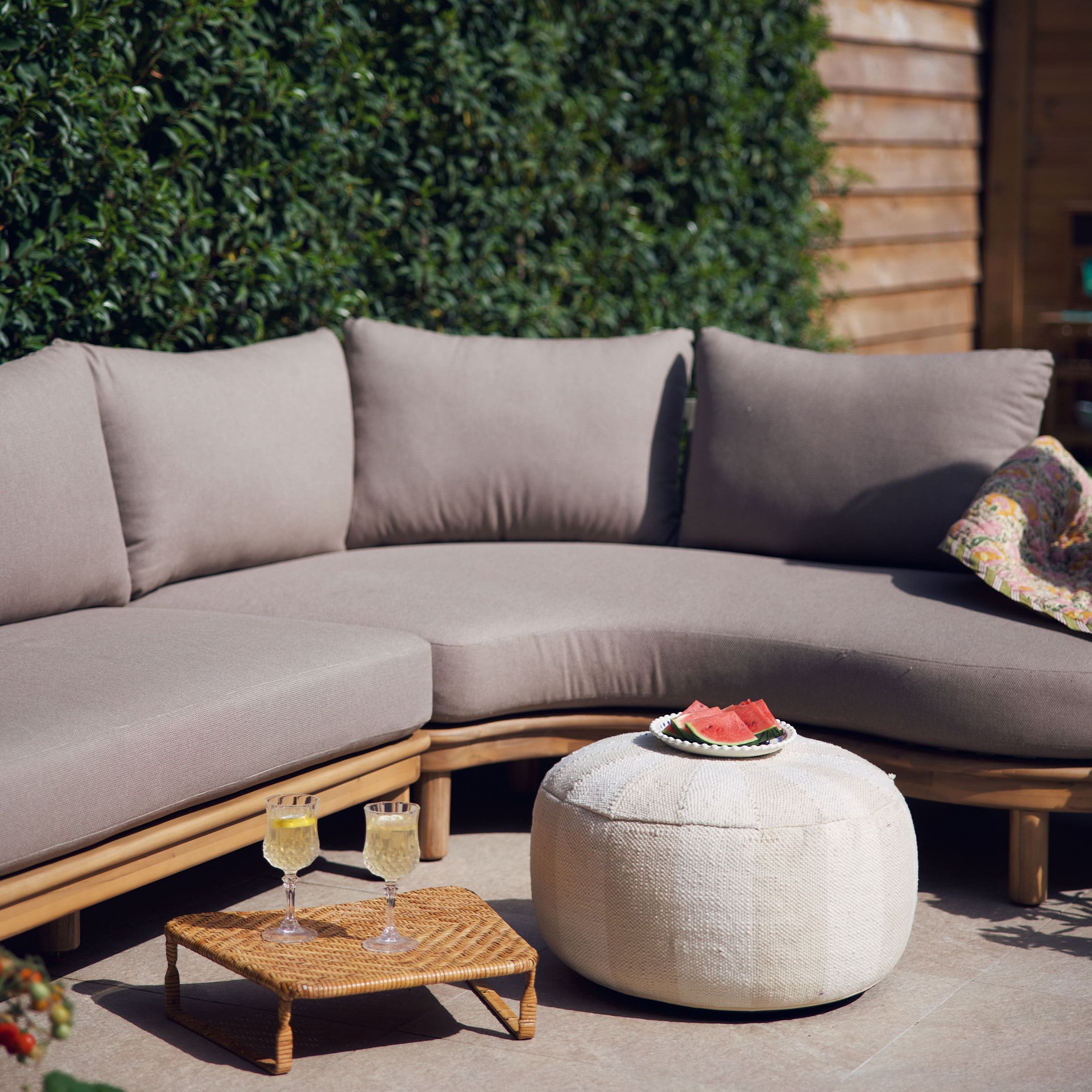 Canapé beige avec coussins sur cadre en bois et pouf blanc sur terrasse décorée pour l'été
