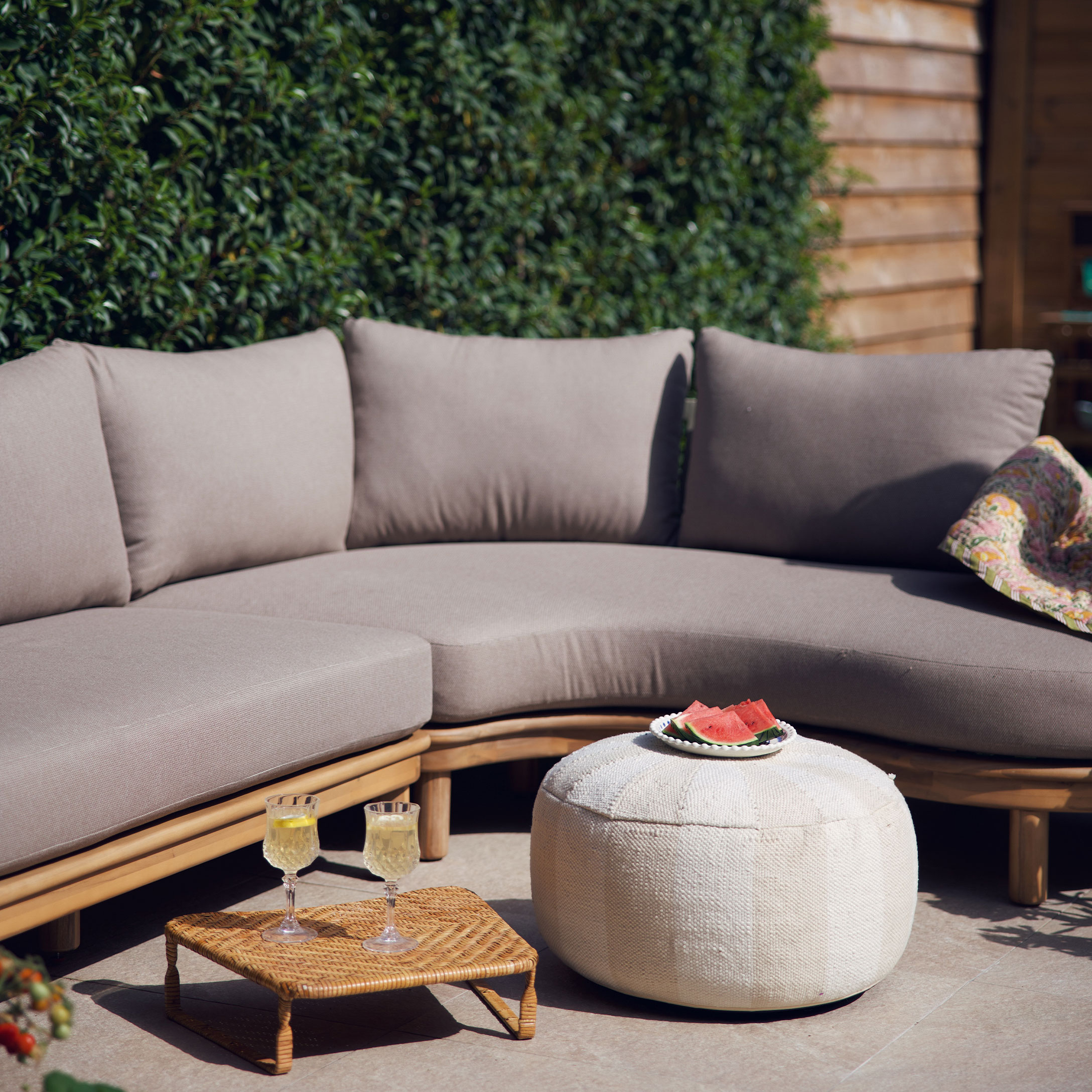 Canapé beige avec coussins sur cadre en bois et pouf blanc sur terrasse décorée pour l'été