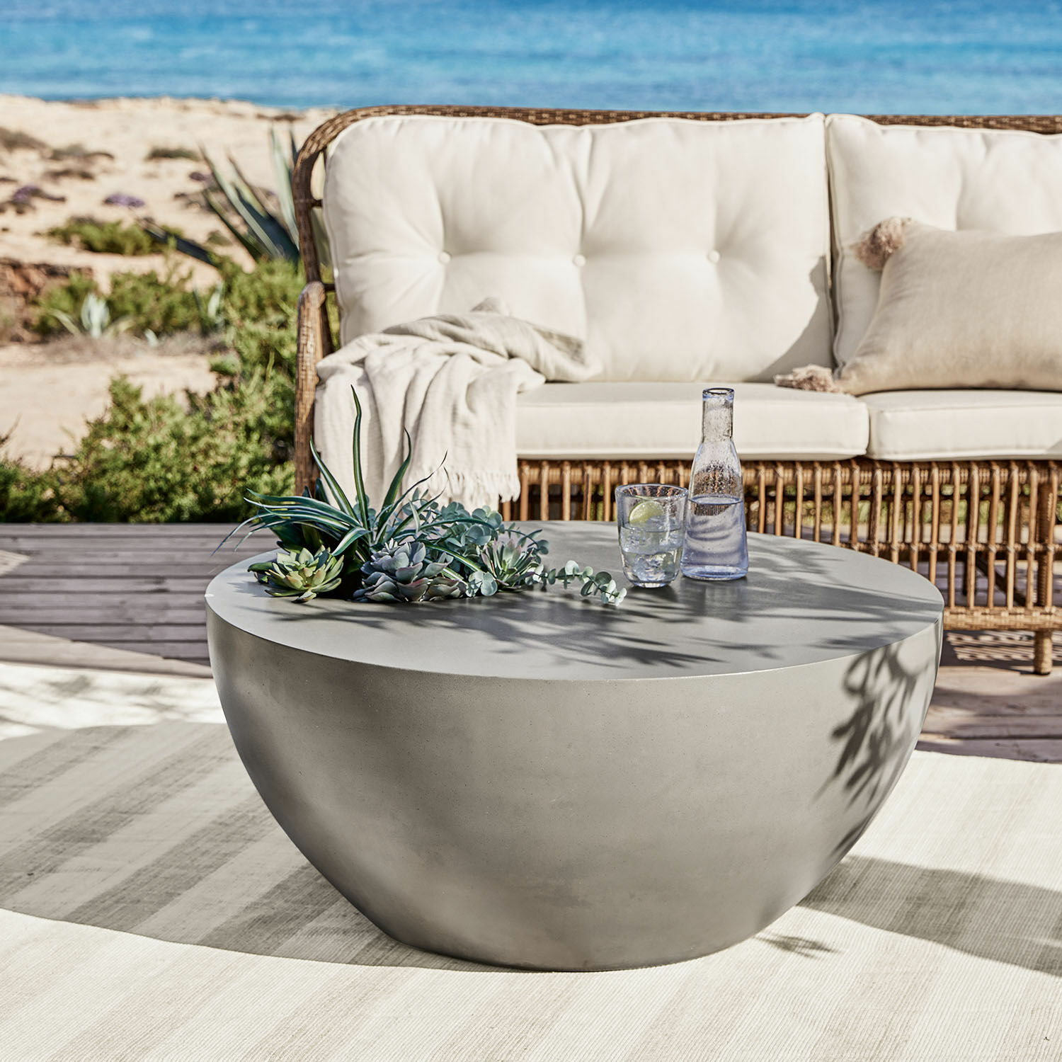 Salontafel Plévin Ronde grijze betonnen salontafel op terras met vetplanten decoratie en glas water