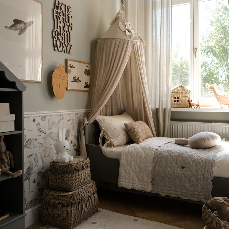 Chambre d'enfant cosy avec baldaquin beige, paniers en osier et lit gris avec literie douce
