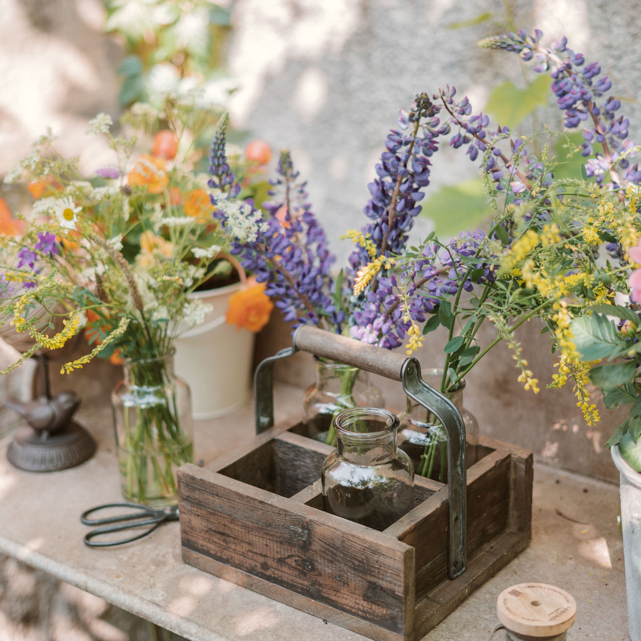 Houten organizer met handvat en glazen vazen met kleurrijke bloemen op een tuintafel