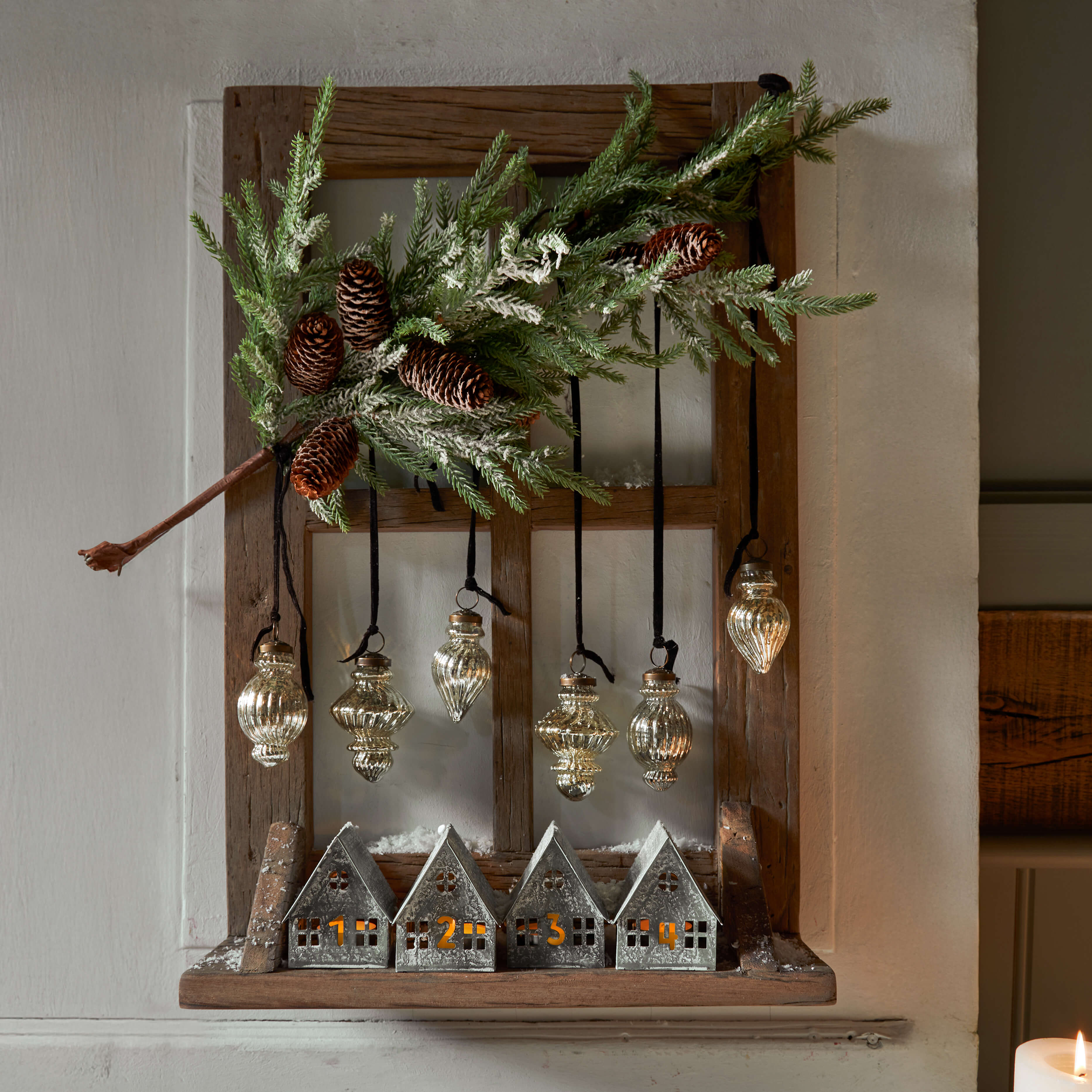 Cadre en bois avec maisons en métal numérotées et décorations en verre suspendues, ornements de Noël avec pommes de pin et branches vertes