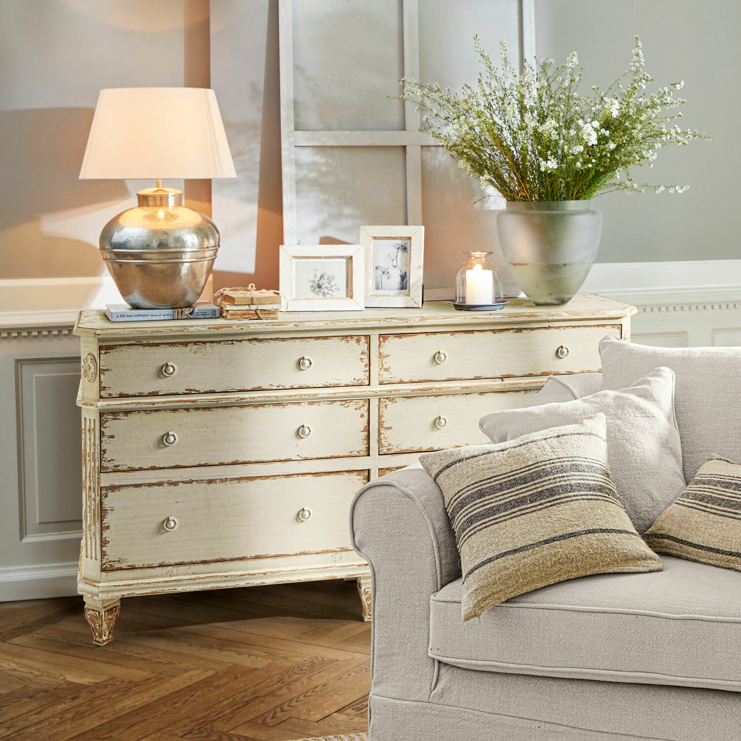 Commode Commeren Commode en bois crème style vintage avec lampe, cadres et décorations dans un salon avec canapé beige