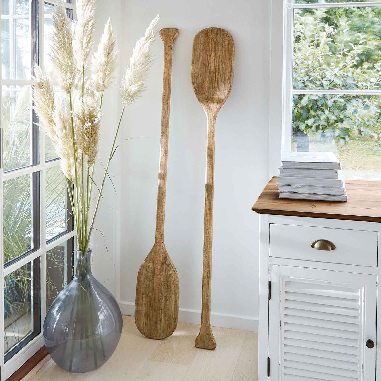 Twee decoratieve houten peddels in natuurlijke kleur tegen een witte muur in een lichte kamer